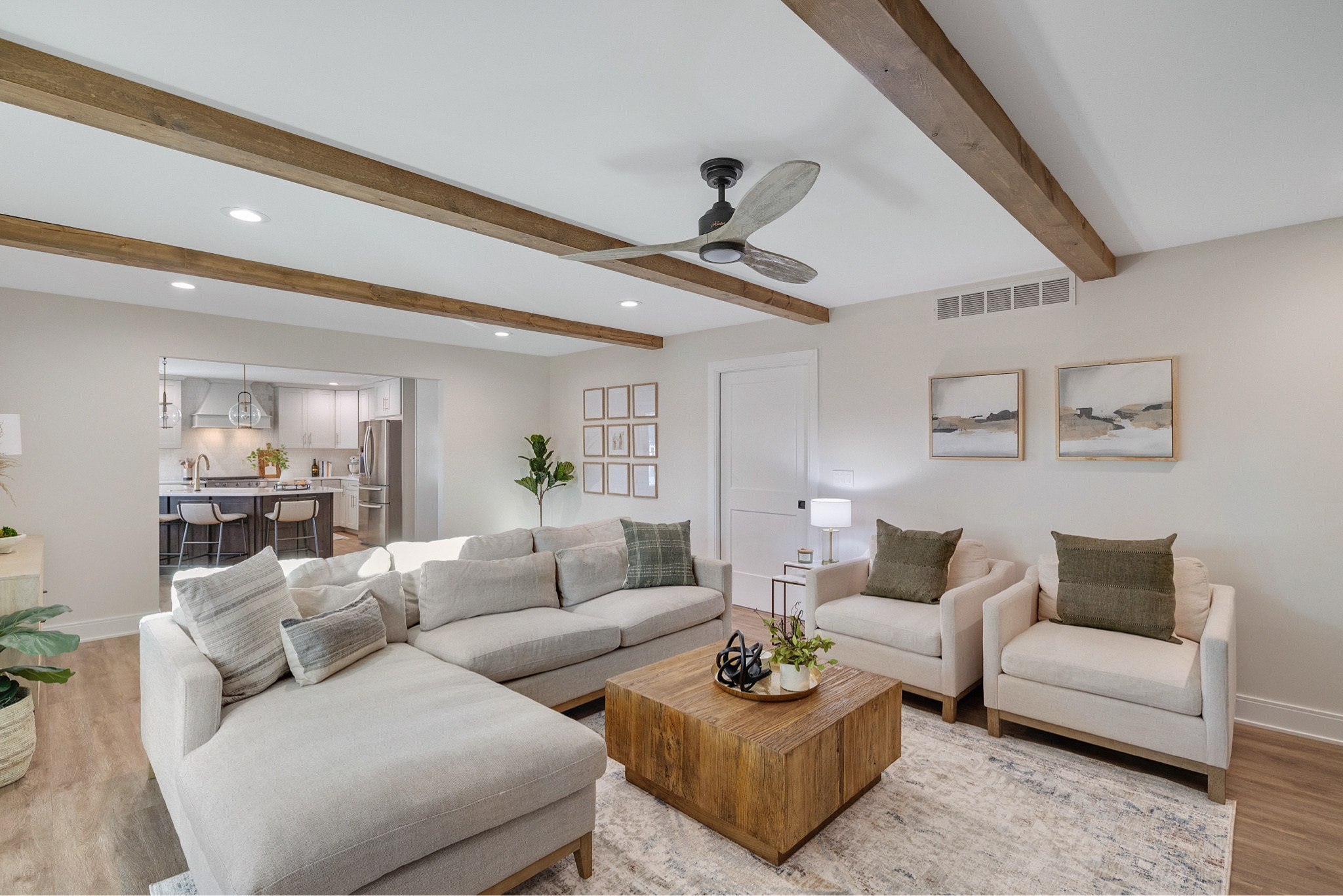 This living room has couch, chairs, coffee table, console table, artwork, ceiling fan, canvas art, large plants, pillows, table decor, tray, sculpture, small potted plant, candle, table lamp, decorative bowl, side table, and wood beams.

#LTKhome