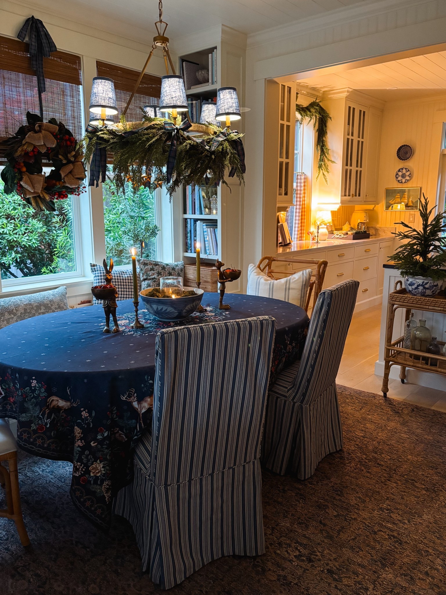 Festive holiday dining room - winter Christmas tablecloth, garland, rattan cart, lamps, wreath, bamboo shades, cafe curtains, brass animal bowls, gold candleholders, chartreuse taper candles, seeded glass hurricane, floating candles, moss balls 

#LTKSaleAlert #LTKHome #LTKHoliday
