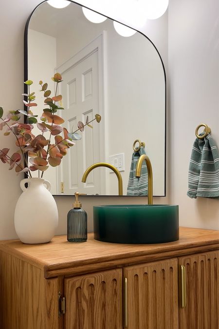 Half Bathroom with wooden vanity and green sink bowl. Brass faucet. Green hand towel. Brass towel ring. Arched mirror. 

#LTKhome #LTKFind