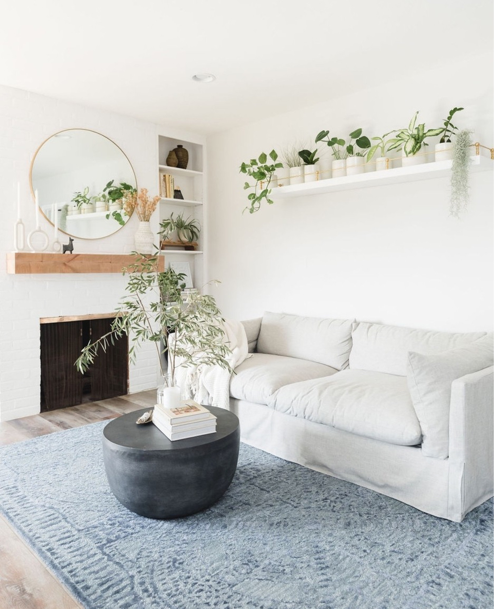 Family room with a slipcovered sofa, blue rug, round coffee table, white floating shelf with brass guardrail, rustic fireplace mantel, round mirror. 

Living room, interior design, home finds, living room decor, home decor, home accessories, farmhouse mantel, floating shelves. 

#LTKFind #LTKhome #LTKstyletip