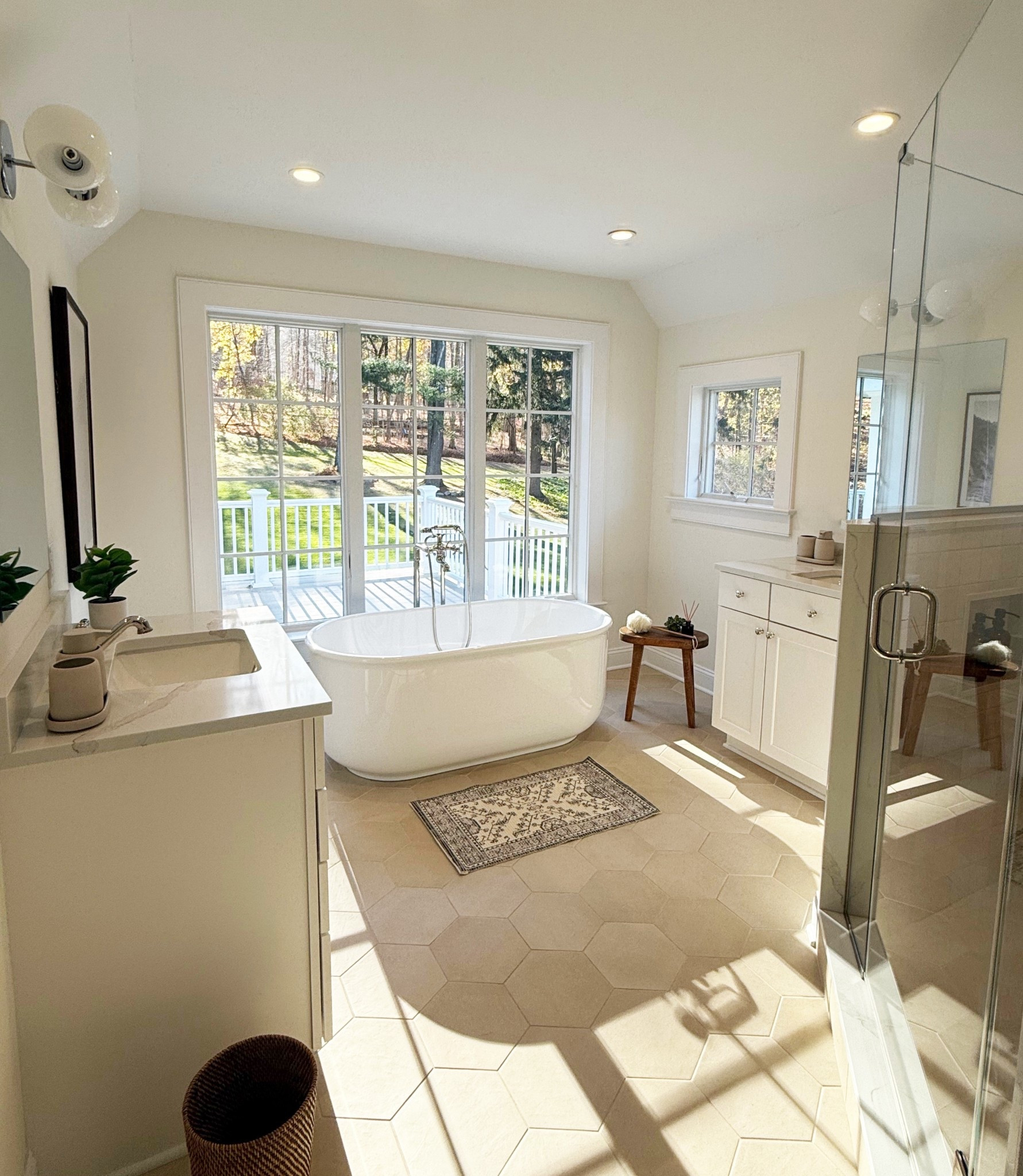 Take a peek at the serene Mount Kisco Estate’s primary bathroom featuring a freestanding soaking tub framed by expansive windows that let in all that natural light!. Hexagon tile flooring, soft neutral tones, and minimalist decor create a spa-like atmosphere. The glass-enclosed shower, marble-topped vanity, and charming wood accents complete the perfect balance of luxury and tranquility.
