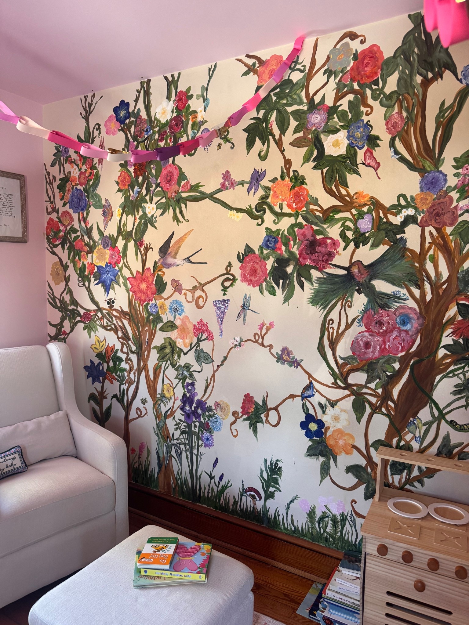 This cozy little corner of my daughter’s nursery has become one of our favorite spots in the house. The hand-painted mural by her Oma adds such a meaningful, personal touch to the space and makes the room feel extra special. Our chic cream rocking chair has quickly become the place for bedtime snuggles, quiet moments, and story time before sleep.

The ottoman is one of my favorite pieces because it’s not only beautiful but also doubles as hidden storage — perfect for tucking away toys and blankets while keeping the space feeling calm and tidy. Right beside it are her three favorite bedtime books that have officially become staples in our nightly routine.

I also handmade the heart paper chains for her birthday, and they ended up being the sweetest decorative detail for the corner. 

And of course, her play kitchen — her newest favorite toy — has quickly become the star of the space and where lots of imaginative play happens throughout the day.

Below are the exact items linked if you’re interested in anything from this cozy little corner. 🌙💕📚


#LTKBump #LTKmomlife #LTKdayinmylife