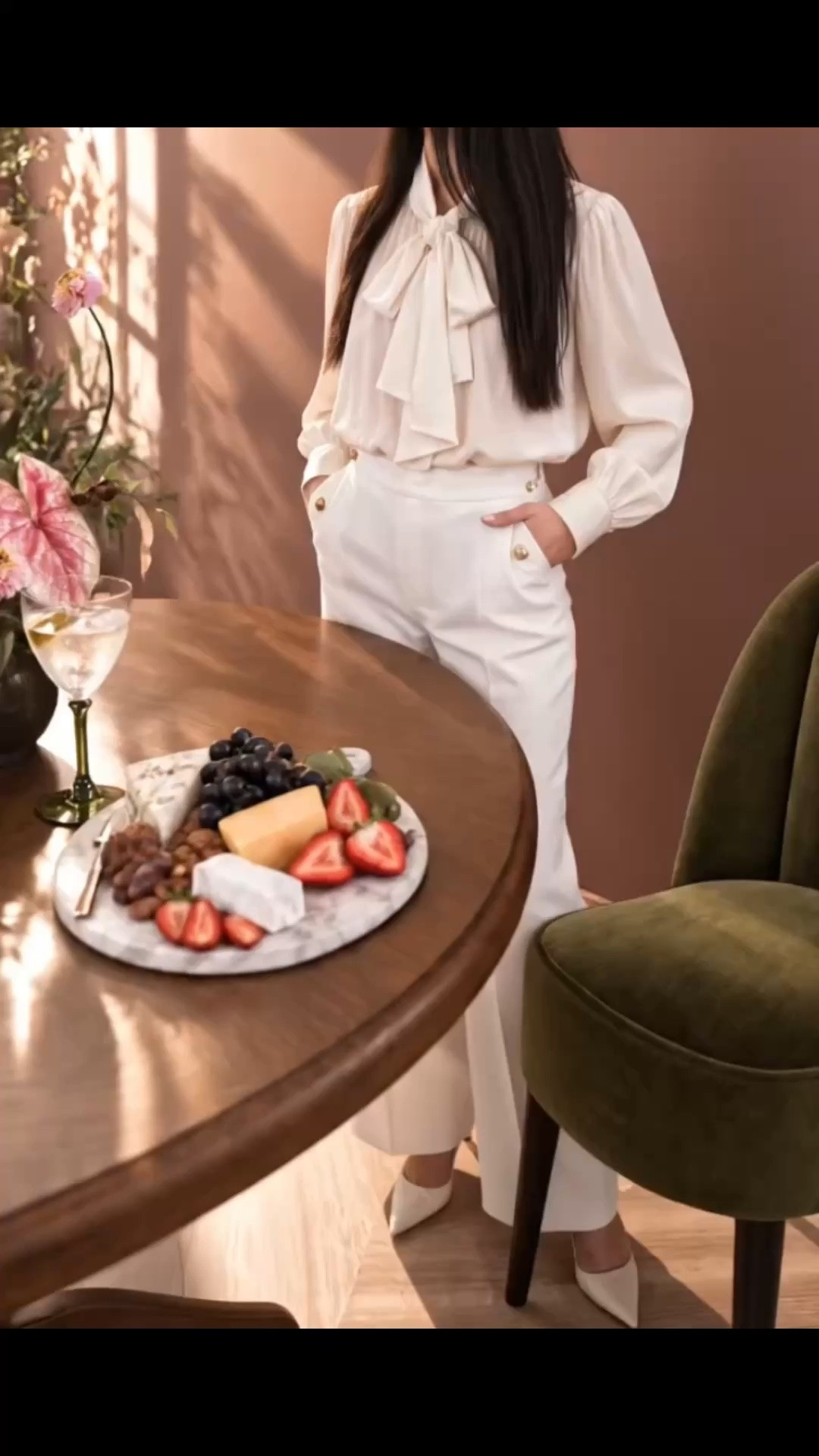 Late-afternoon cocktail time at home—one of those quiet little moments when the breakfast nook or kitchen nook becomes the perfect place to slow down, unwind, and ease into the evening.

I love the Warby Round Dining Table for its beautifully understated presence. Crafted with solid oak and oak veneer, the rich mocha-toned wood brings out the natural grain in such a calm, sophisticated way. The rounded silhouette and clean pedestal base keep it streamlined and modern, while all that warm wood still makes the space feel grounded and inviting.

The Arco Channel Dining Chair is such a beautiful pairing. I especially love the deep green upholstery and the elegant channel detailing across the back. The silhouette feels tailored, clean, and modern, but still soft and comfortable enough for a relaxed dining nook. Against the warm oak table, that rich green adds just the right amount of depth.

I kept the fashion crisp and light with the ivory bow blouse and tailored white trousers, creating a fresh contrast against the deeper wood, olive green, and romantic muted rose wall. In the late-afternoon sunlight, that rose tone feels especially soft and atmospheric—almost like bringing a little bit of sunset indoors.

Add a delicate flower arrangement, green-stemmed cocktail glasses, and a charcuterie board, and this becomes such an inviting spot to pour a cocktail, sit down, and enjoy that quiet transition from afternoon into evening.

#BreakfastNook #KitchenNook #WarbyDiningTable #RoundDiningTable #OakDiningTable #ArcoDiningChair #ChannelDiningChair #DiningChair #CocktailGlass #Stemware #CharcuterieBoard #FlowerArrangement #Blouse #WhiteTrousers #ModernDining #ModernHome #HomeDecor #LTKStyle

#LTKHome #LTKHome #LTKSaleAlert #LTKdayinmylife
