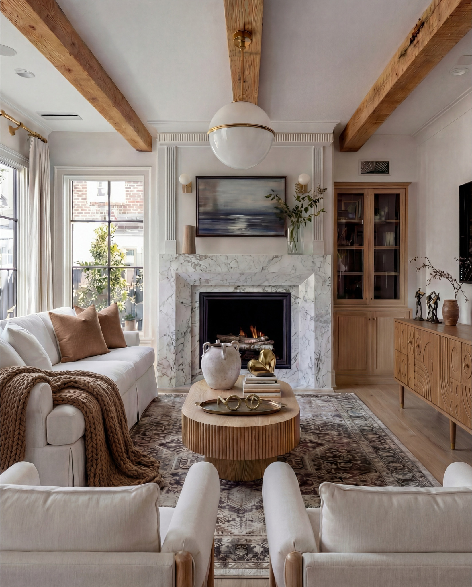 Shop the Look:
• White upholstered sofa (clean-lined, low profile)
• White upholstered armchairs (pair)
• Light wood round coffee table (fluted or ribbed base)
• Neutral vintage-style area rug (muted brown and beige tones)
• Marble fireplace surround
• Black fireplace insert
• Large framed landscape wall art (soft blue and neutral tones)
• Brass wall sconces (pair, globe style)
• White globe pendant light with brass detail
• Natural wood ceiling beams
• Light wood flooring

Coffee Table Styling:
• Large white ceramic vase (rustic sculptural style)
• Decorative hardcover books (neutral covers)
• Gold abstract heart sculpture
• Brass oval tray
• Decorative brass object (sculptural accent)

Sofa Styling:
• Neutral throw pillows (warm beige)
• Chunky knit throw blanket (camel or warm brown)

Media Console Area:
• Light wood sideboard / media console (carved front detail)
• Brass cabinet knobs
• Black figurine sculptures (musician figures, set of three)
• Brown ceramic vase
• Dried branches / minimalist floral stems
• Brass decorative tray

#LTKHome #LTKFindsUnder100 #LTKSaleAlert
