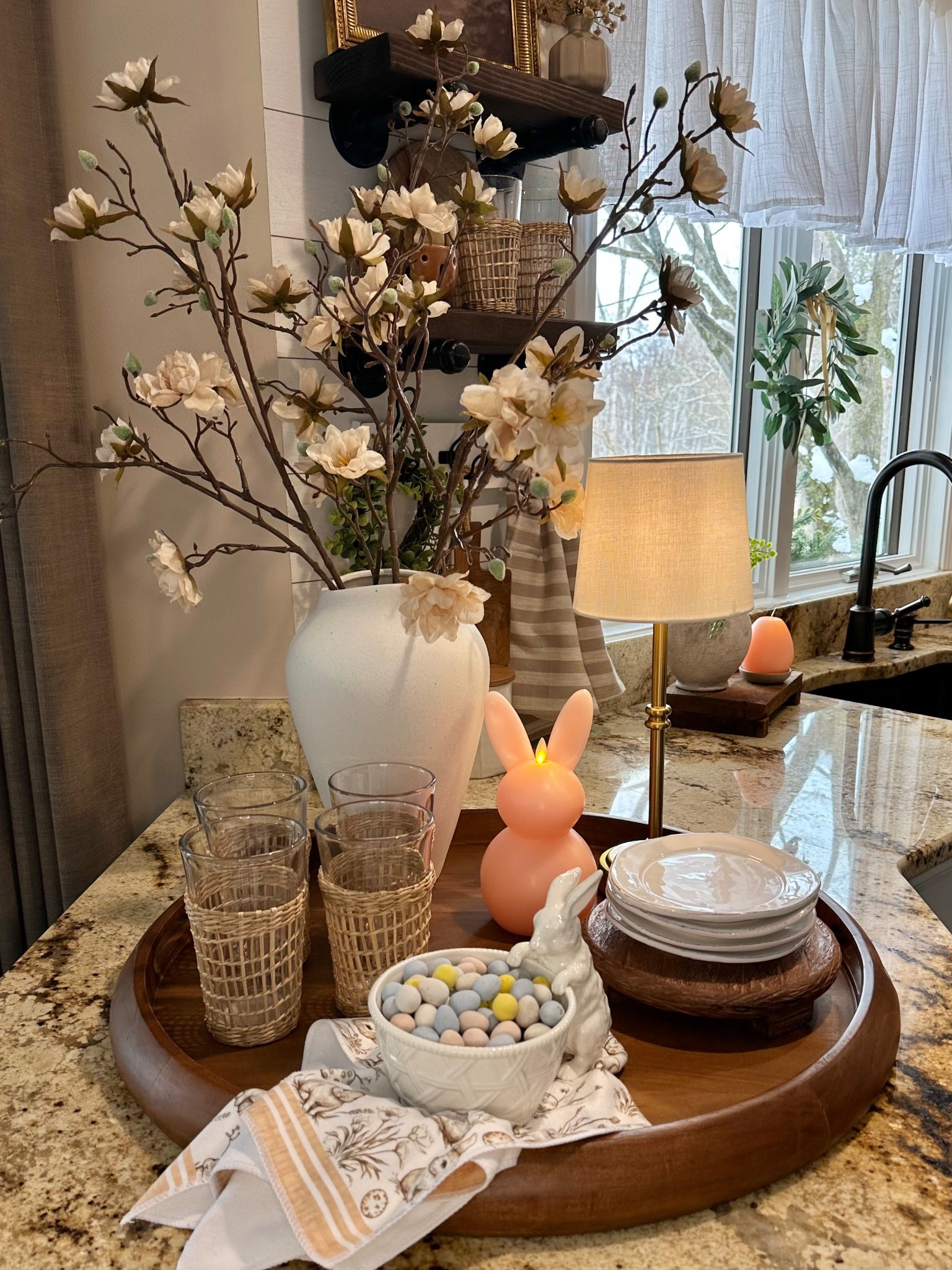 Spring | Easter Centerpiece. Follow @farmtotablecreations on Instagram for more cozy home inspiration 🤍

A functional centerpiece that doubles as everyday convenience ✨ This warm wood tray keeps essentials beautifully contained while adding soft spring charm to the kitchen. Three faux magnolia stems in a neutral vase create height and texture, while the woven-wrapped glasses, stacked plates, and linen napkin make it easy to grab what you need for casual meals or entertaining. The soft glow of the flameless bunny candle and pastel candy bowl add a subtle Easter touch without feeling overdone — cozy, practical, and pretty all at once.

#traydecor #centerpiece #kitchendecor #springdecor #easterdecor #countertopdecor #servingtray #fauxflorals #kitchenstyling #tabledecor #homeaccessories

#LTKSeasonal #LTKSaleAlert #LTKHome