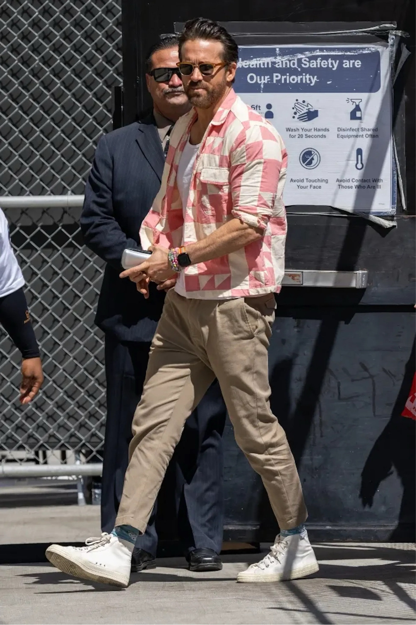 Ryan Reynolds on his way to film Jimmy Kimmel wearing a pink quilt l/s shirt, khaki pleated chino pants, and white high tops. 