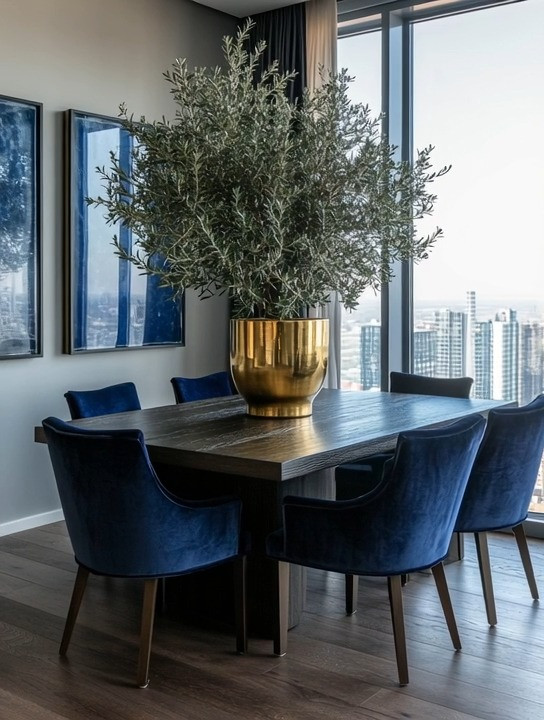 Choose the table for how you actually live. 🤎

A dining table isn't furniture, it's where the days land. Homework, holidays, long dinners that turn into longer conversations. Dark wood grounds all of that. It holds the room the way a good host holds a table.

Then soften it. Navy velvet chairs against hard wood is one of my favorite contrasts. The velvet changes the mood around the wood, and because the chairs don't match the table, the room feels collected instead of copied.

Every dining room needs something alive and something warm. An olive tree in an oversized gold planter gives you both. Greenery and warm metal, one move.

I've linked dark wood tables, navy velvet chairs, and large gold planters to recreate the look. 

 #elegantanddriven #diningroomdecor #velvetchairs #homestyling #interiordecor