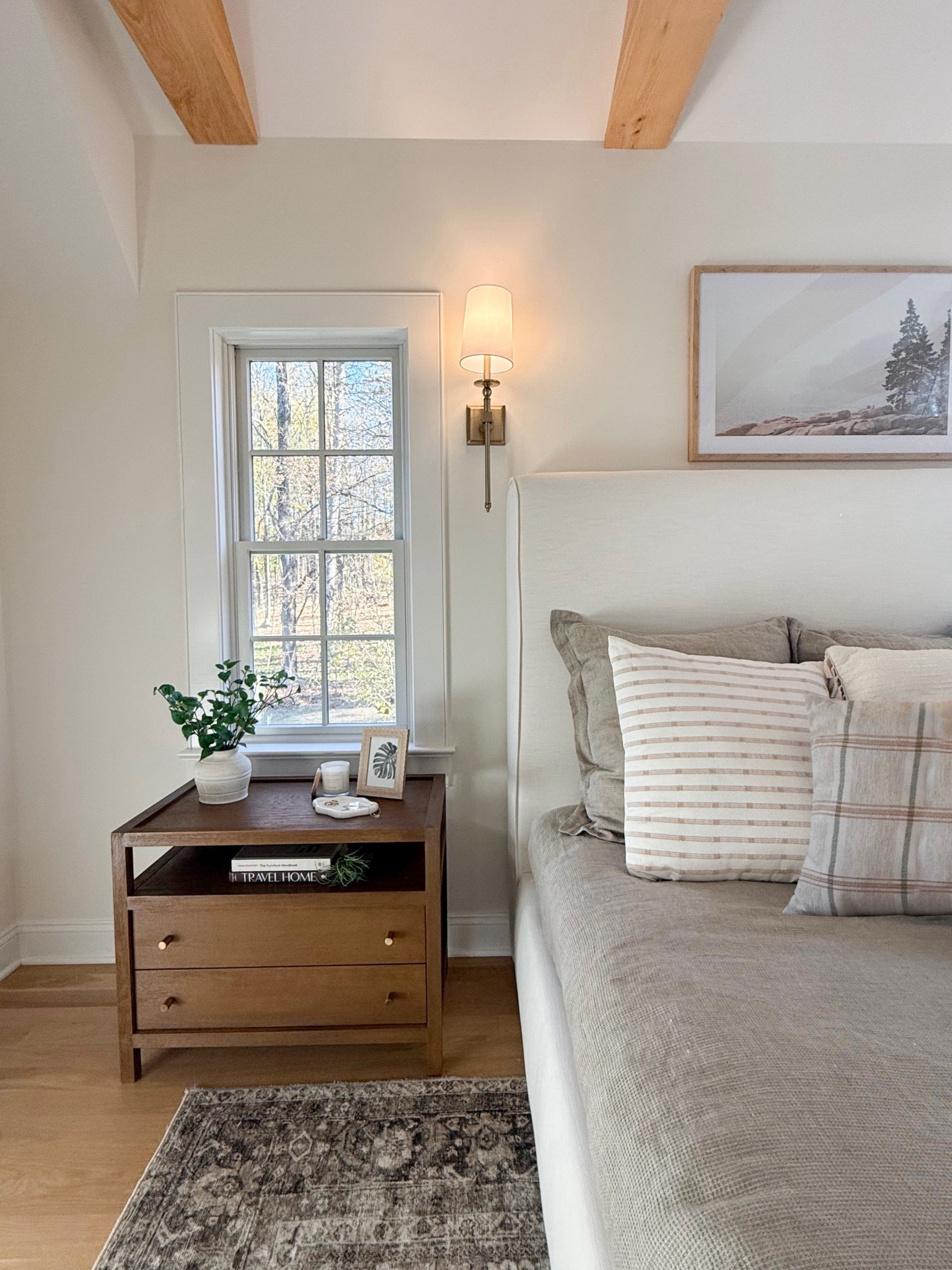 A side view of the bedroom captures the inviting charm of the bed paired with a beautifully styled nightstand. The soft, layered bedding cascades down in cozy textures, while the nightstand holds a curated mix of essentials. The warm wood tones and subtle lighting create a serene and restful atmosphere, perfect for winding down. 
