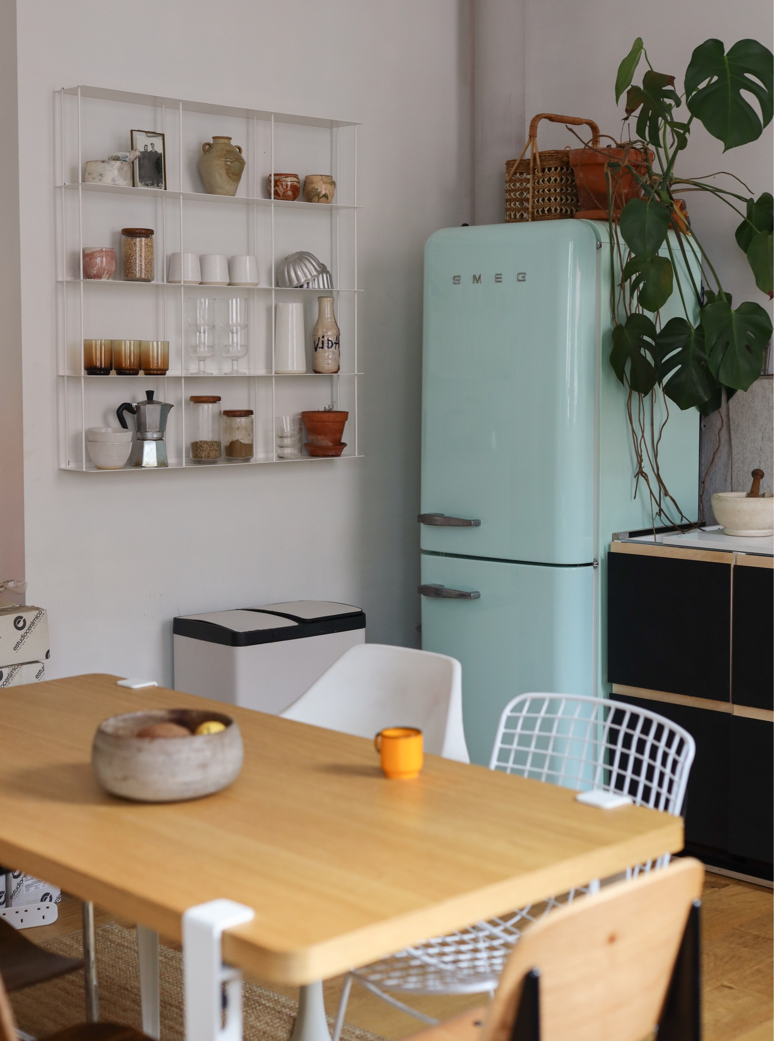 Light and airy kitchen in a converted factory apartment. Light blue/ pastel green retro Smeg fridge freezer. Open white wire shelving with collected glassware and jars. TipToe table and black Plykea kitchen cupboards. Monstera plant.

#LTKeurope #LTKhome