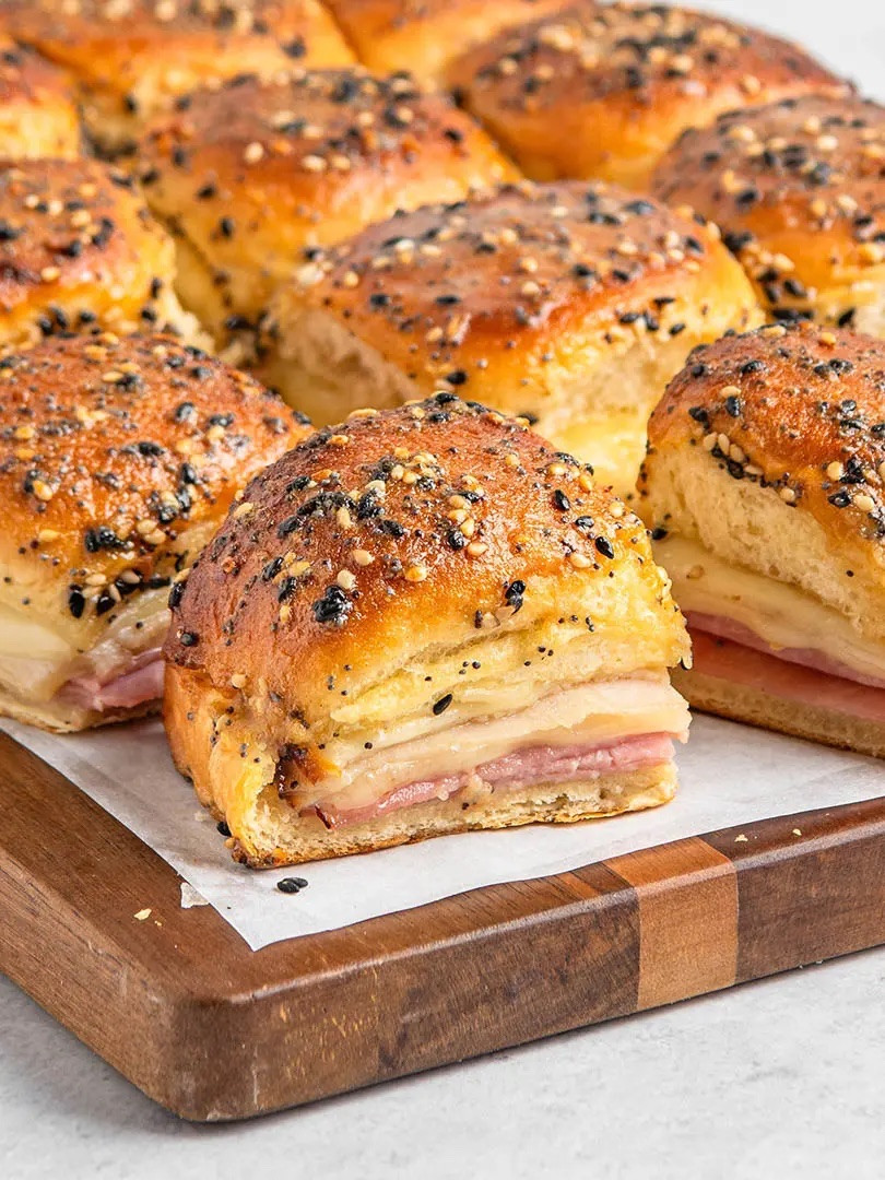 Ingredients
* 1 (12-roll) package King's Hawaiian Original Hawaiian Sweet Rolls
* 6 slices ham halved
* 6 slices Swiss cheese halved
* 6 slices turkey halved
* 6 slices provolone cheese halved
* 4 tbsp unsalted butter
* 2 tbsp honey
* 2 tbsp everything bagel seasoning
* 1 1/2 tbsp Dijon mustard
* 1 tsp flaky salt (I like Maldon)
Instructions 
* Preheat the oven to 350 degrees. 
* Remove rolls from package without breaking them apart into individual rolls. Slice crosswise to create a top and bottom layer. Arrange the bottom layer on a rimmed baking sheet. Top with ham in an even layer, then add even layers of Swiss, turkey, and provolone. Place the top layer of rolls over the ham and swiss. 
* Microwave the butter in a small microwave-safe bowl until melted. Once butter has melted, stir in honey, seasoning, and mustard. Drizzle or brush over tops of rolls. 
* Bake sandwiches until tops are golden brown and cheese is melty, about 15 minutes. 


#LTKfoodie #LTKSeasonal