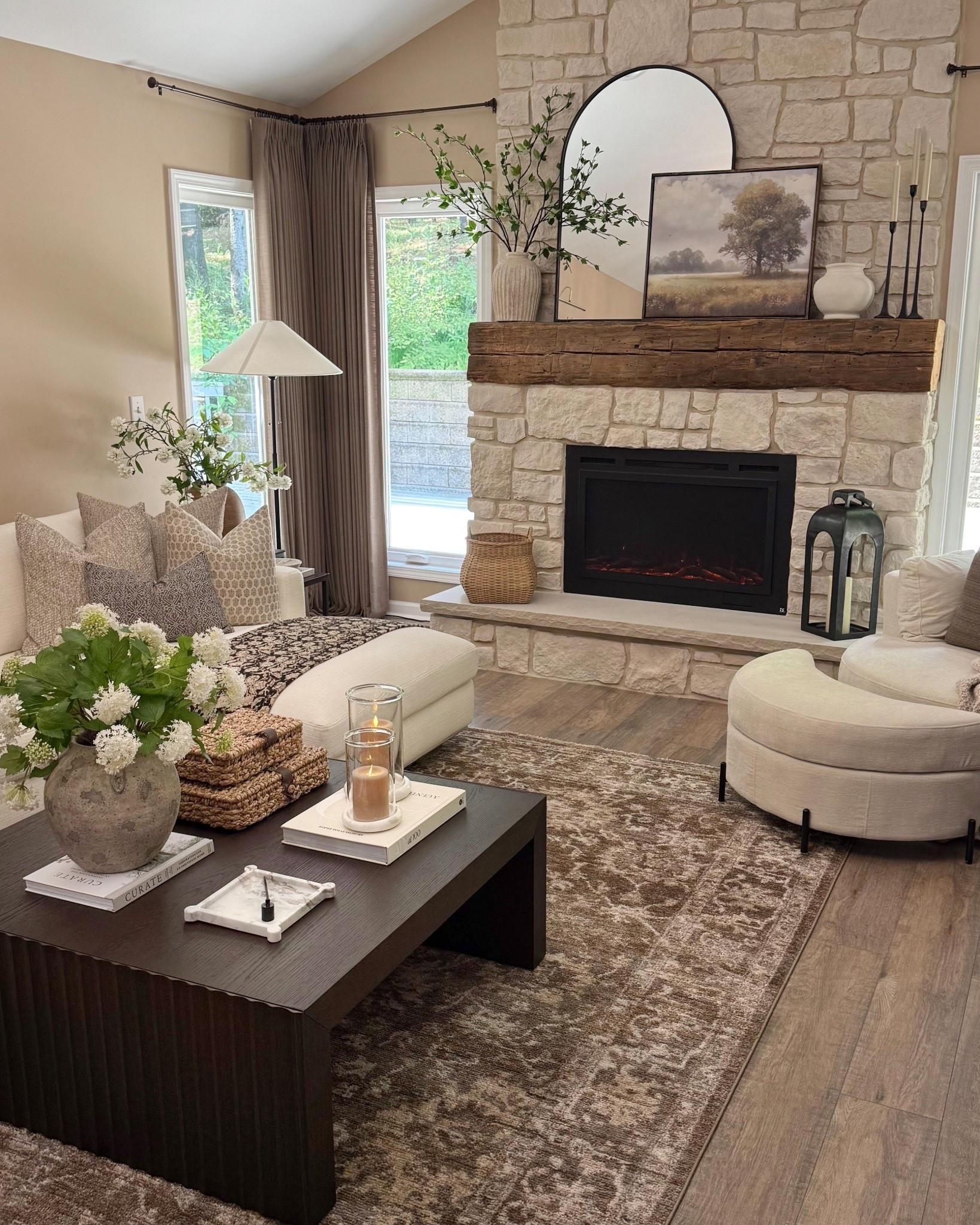 Cozy Living Room View  Follow @farmtotablecreations on Instagram for daily home inspiration and shoppable finds.

This living room is all about warmth, texture, and balance. The full stone fireplace adds timeless character, layered with a rustic wood mantel, oversized round mirror, and soft neutral art for an elevated focal point. A vintage-inspired neutral rug grounds the space, while the curved accent chairs and plush sectional create an inviting, conversational layout. Finished with a sculptural coffee table, soft textiles, and cozy lighting, this space feels calm, intentional, and lived-in without feeling busy.

#livingroom #sectional #accentchairs #neutralrug #arearug #coffeetable #fireplace #livingroomfurniture #homedecor #interiorinspo

#LTKSeasonal #LTKHome #LTKSaleAlert