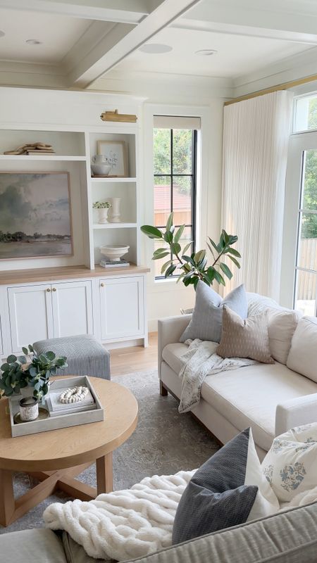 Shop our great room! I love our cream sofa from joss and main (a great dupe for the Pottery Barn Jake sofa!) blue and neutral throw pillows, ivory linen curtains, white TV unit, round light wood coffee table 