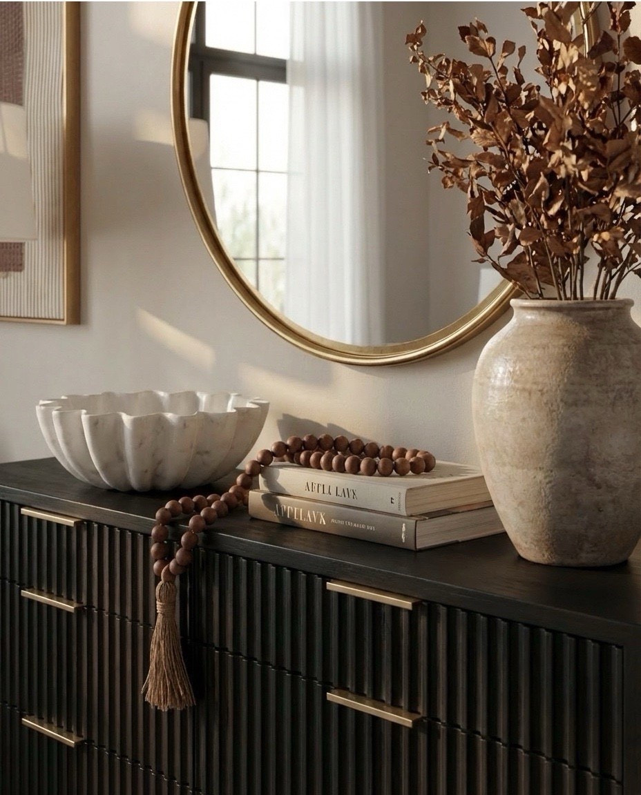 Shop the Look: Bedroom Refresh
• Dark wood bed frame with curved headboard
• Crisp white bedding set (duvet + sheets)
• Warm brown accent pillows
• Textured knit or woven throw blanket (camel/brown)
• Ivory boucle bench stools (set of two)
• Vintage-style patterned area rug (neutral brown + taupe tones)
• Wood nightstands with drawers
• Table lamps with white drum shades
• Wall sconces with brass detail
• Framed landscape artwork above bed
• Organic-shaped wall mirrors (brass frame)
• Black fluted dresser with brass hardware
• Round brass wall mirror
• Sculptural white ceramic bowl
• Decorative books with wood bead garland
• Neutral ceramic vase with dried branches
• Upholstered accent chair (cream fabric, wood frame)
• Slim brass floor lamp with white shade

#LTKSaleAlert #LTKHome