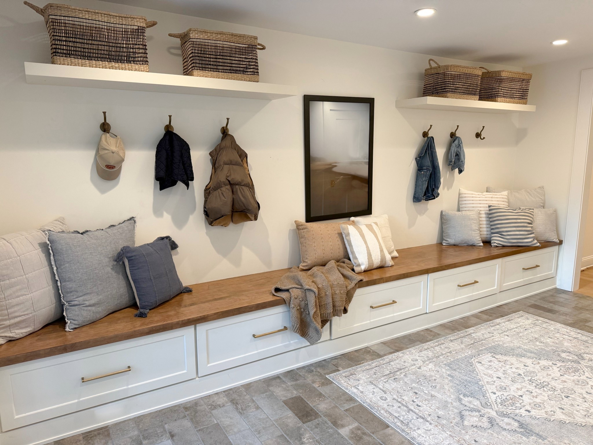 A charming and functional mudroom just off the back door, featuring striking blue stone floors that ground the space with natural elegance. A long built-in bench offers both seating and smart storage below, while a row of hooks keeps coats and bags organized. Open shelving above adds a touch of rustic charm adds warmth and personality to this welcoming entryway! 
