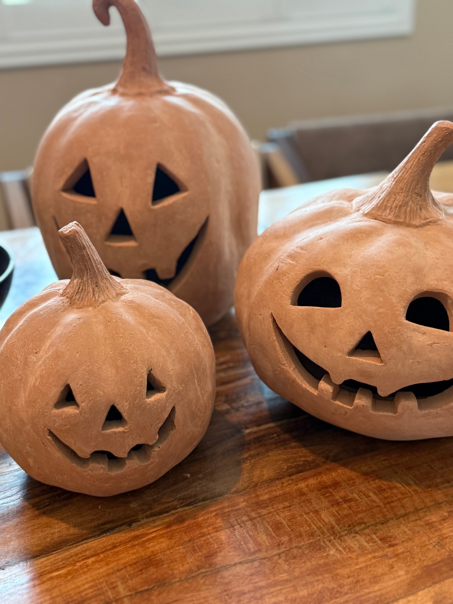 Three terracotta pumpkins with carved jack-o’-lantern faces sit on a wooden table, each one grinning a little differently — like they’re plotting something cute but slightly chaotic. 

#LTKHome #LTKSeasonal
