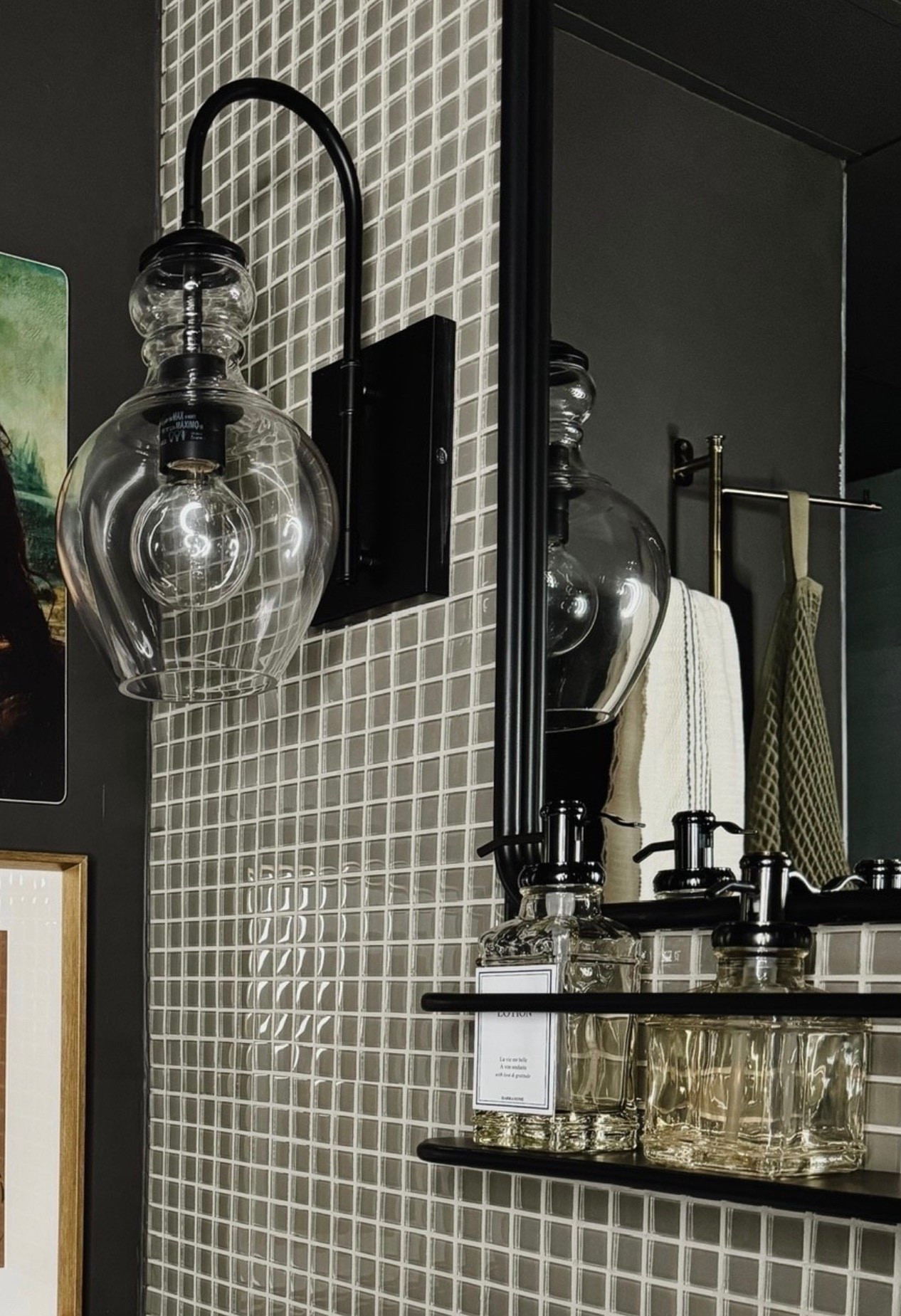 Moody bathroom styling done right 🖤 This space features a sleek black wall sconce, a clear glass globe light, and a textured square tile backsplash that adds depth and shine. The arched metal sconce arm, black framed mirror, and modern bathroom shelf keep things clean and architectural, while the glass soap dispensers, apothecary bottles, and neutral hand towels bring in that curated, lived-in feel. A perfect mix of modern bathroom design and classic details.

#eanesinteriors #bathroominspo #bathroomdesign #modernbathroom #moodybathroom #blacksconce #glassglobelight #tilebacksplash #bathroomshelf #soapdispensers #apothecaryjars #bathroomdecor #ltkhomestyle

#LTKOver40 #LTKHome #LTKSeasonal