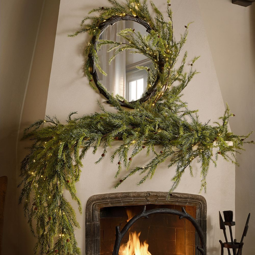 A long, loose garland of faux branches draped across a mantel above a lit fire