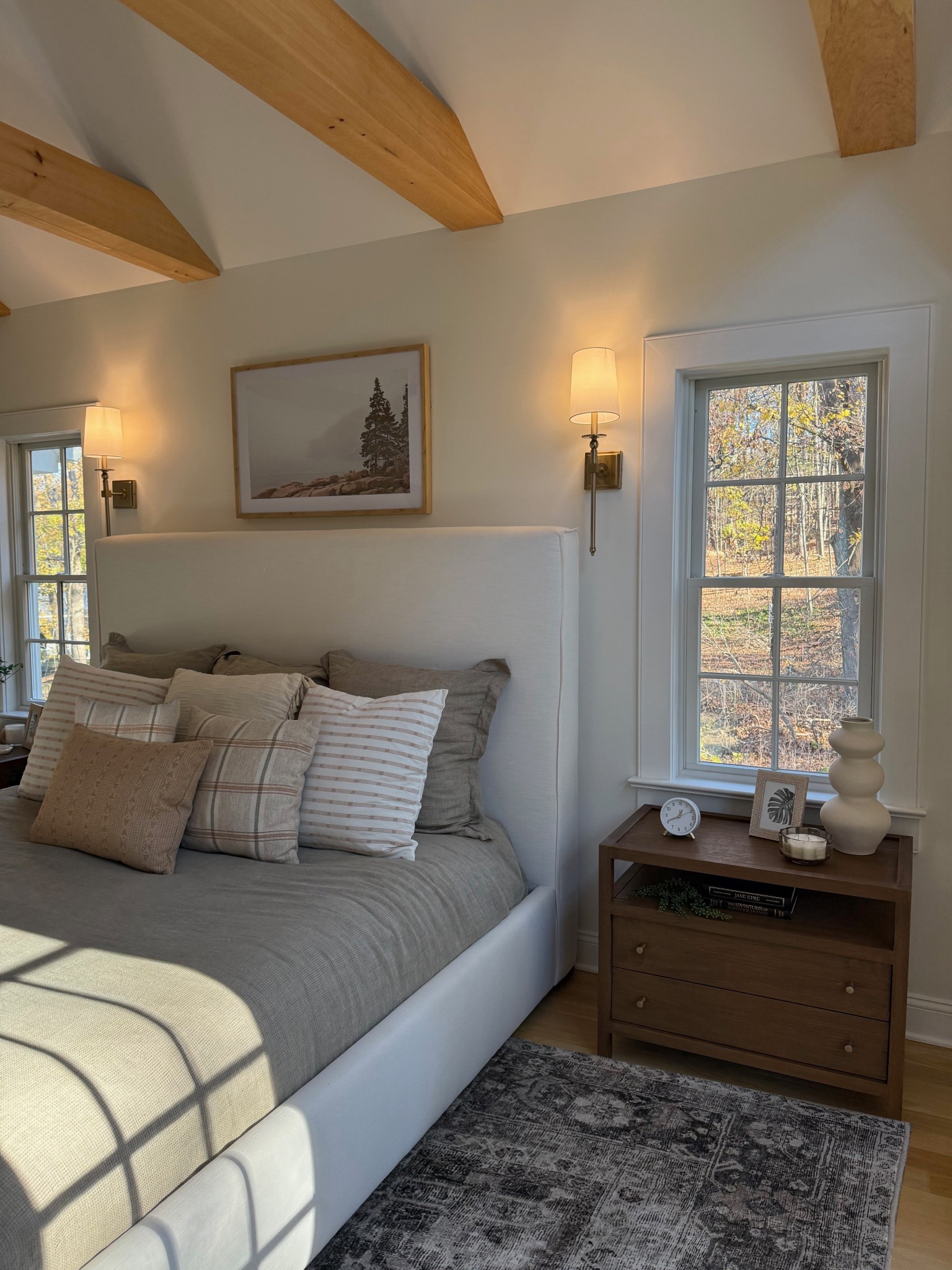 A head-on view of the bedroom highlights the elegant headboard as the focal point, upholstered in a soft, neutral fabric that adds texture and warmth. Flanked by matching nightstands and sleek wall sconces, the bed is layered with cozy linens, plush pillows, and a relaxed, sophisticated vibe. The composition creates a perfectly balanced and inviting retreat, blending comfort with timeless design.
