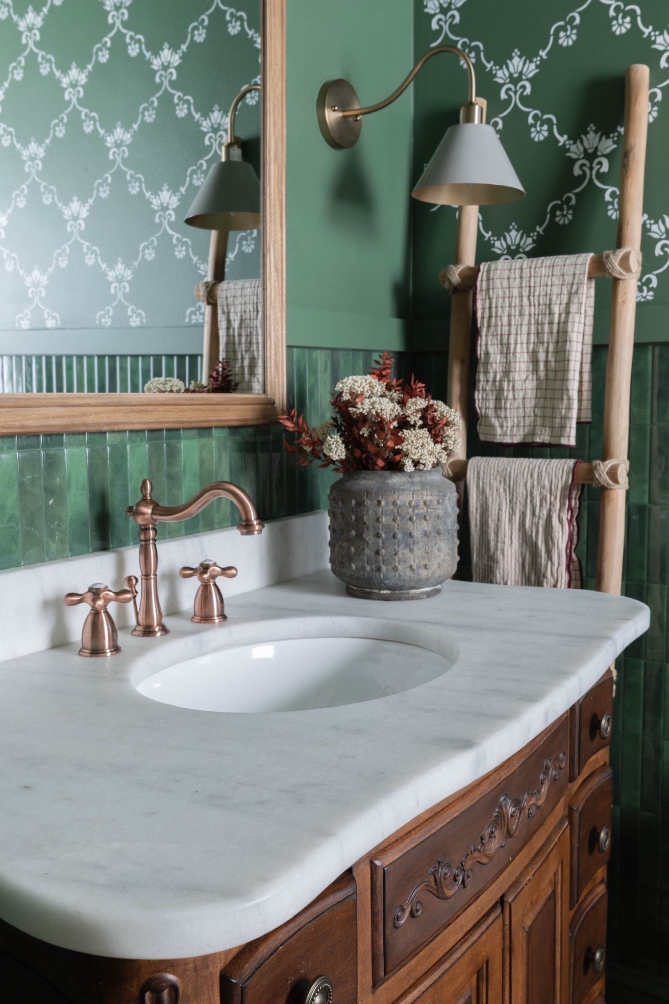 A collected and cozy bathroom ✨ Featuring a classic wood vanity with carved details, topped with a marble countertop and bronze faucet hardware. Green wall tile and wallpaper add richness, complemented by wall sconces, a rustic towel ladder, and a textured vase overflowing with dried blooms. 🌿
#BathroomDecor #WoodVanityStyle #MarbleSink #BronzeHardware #GreenTileWall #PatternedWallpaper #RusticTowelLadder #DriedFlowerArrangement #eanesinteriors



#LTKdayinmylife #LTKFindsUnder50 #LTKHome