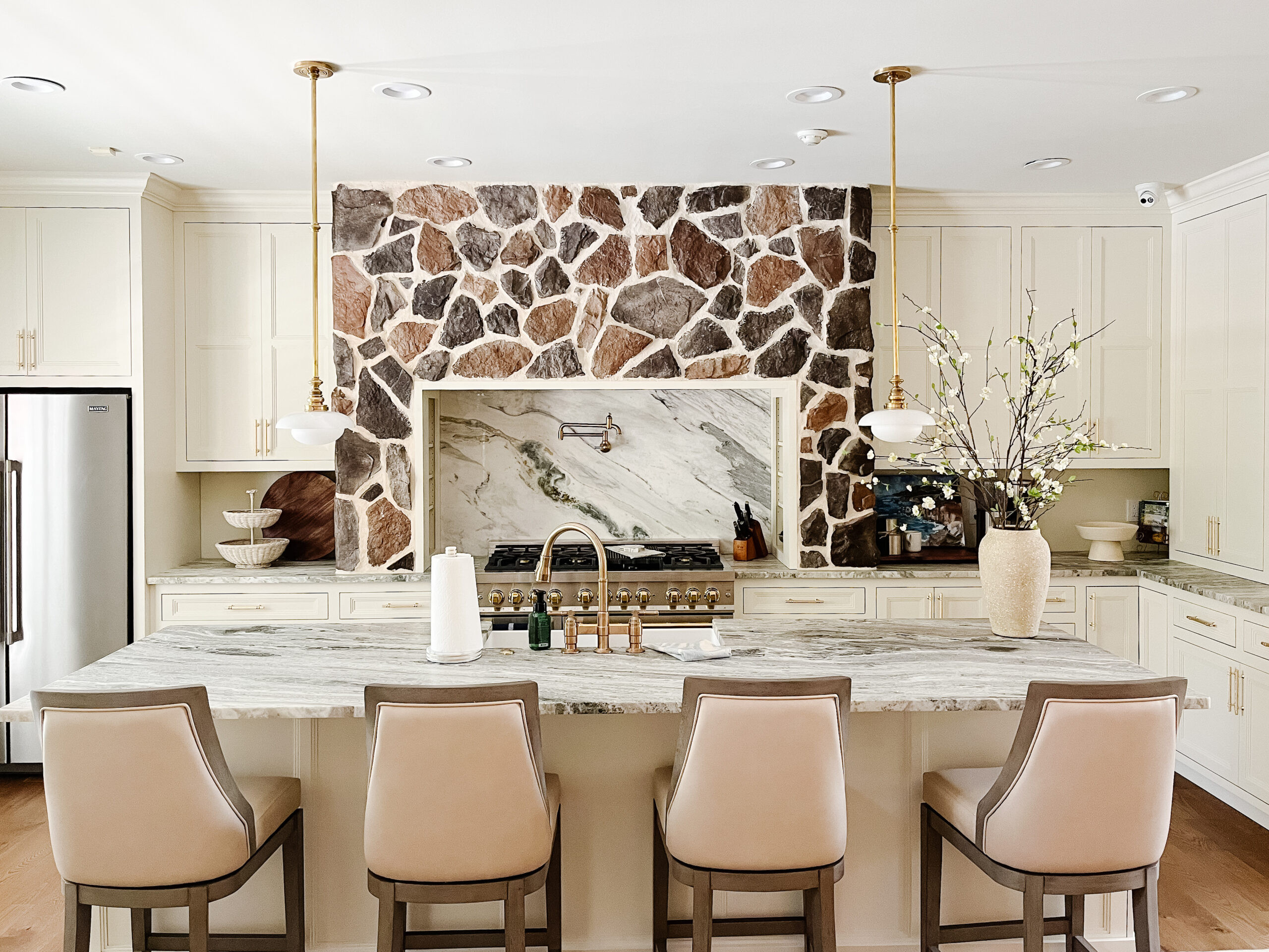 Open sightlines, layered texture, and timeless finishes ✨ Removing the wall completely transformed the energy of this home, and that stone range hood steals the show. Soft-veined quartz with a full-height slab backsplash keeps everything feeling seamless, while ceiling-height cabinetry, classic pendants, and upgraded appliances bring a modern polish that still feels warm and livable. Shop a similar look for your own kitchen refresh below. 🤍 

 #LTKHome