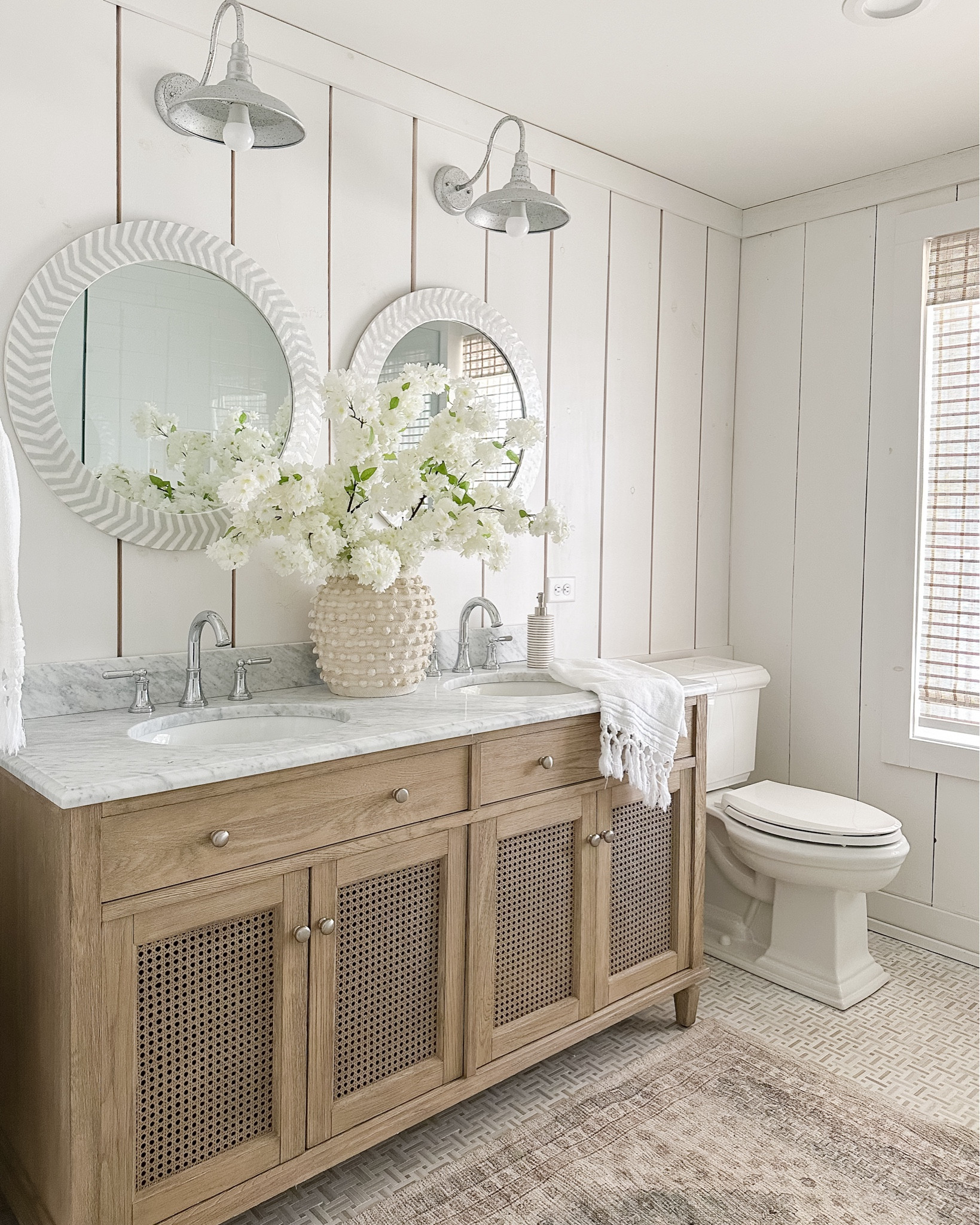 Spring bathroom🌸 
*Vase and florals coming soon to onecottageway.com!
…
Spring decor, cherry blossoms, Bathroom vanity, double sink, coastal, cane cabinet doors, neutral home decor, lake house, round mirror, roman blinds

#LTKhome #LTKSeasonal