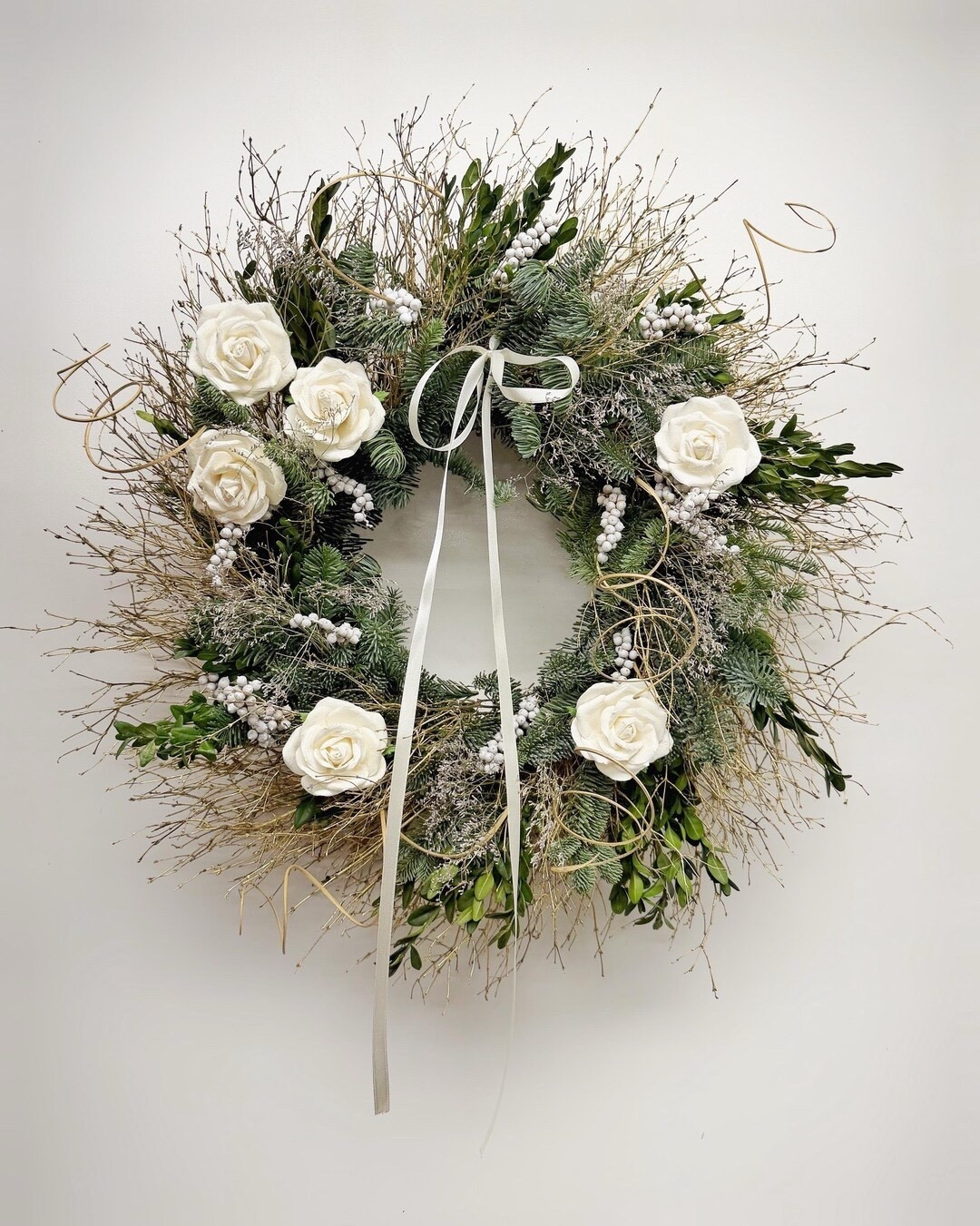 Welcome the New Year with this luminous winter wreath that blends fresh evergreens and elegant details for a timeless seasonal statement. Fragrant noble fir and glossy boxwood create a full, classic base, accented with white paper roses, delicate caspia, gold twigs, and softly painted white berries for a subtle sparkle. Finished with a flowing satin bow, this handcrafted wreath feels romantic, festive, and perfectly wintery—ideal for greeting guests with warmth and style throughout the season.

#LTKhome #LTKseasonal #WinterWreath #NewYearsDecor #FrontDoorDecor #HolidayHome #EtsyFinds #WinterDecor #FestiveHome

#LTKSeasonal #LTKHoliday #LTKHome