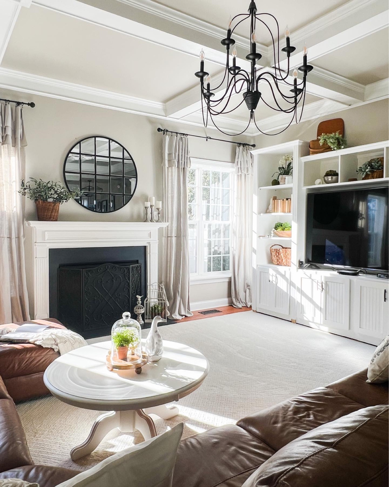 Get ready for spring or summer with this light and natural decorating style. Transitional home decor with revere pewter walls, drop cloth curtains, gas fireplace with painted marble surround, large round mirror, black iron chandelier, round white coffee table.

#LTKhome