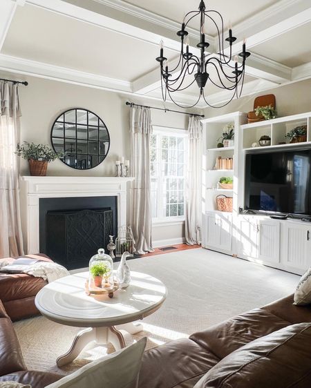 Get ready for spring or summer with this light and natural decorating style. Transitional home decor with revere pewter walls, drop cloth curtains, gas fireplace with painted marble surround, large round mirror, black iron chandelier, round white coffee table.

#LTKhome