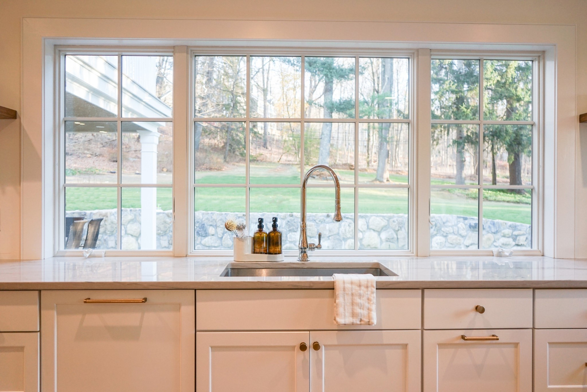 You won’t get tired of doing dishes here! A peaceful kitchen view from the sink, gazing out through a large window into serene wooded land, blending nature with the heart of the home. 