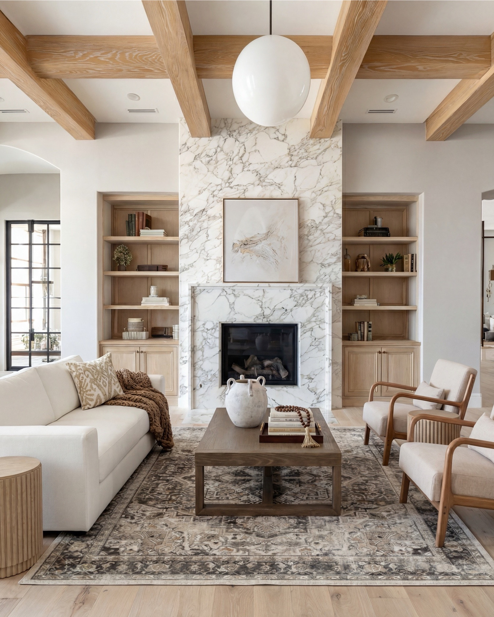 This living room is giving warm modern luxury in the softest, most elevated way. The marble-wrapped fireplace instantly becomes the star—clean, dramatic, and so timeless—and the light oak built-ins on both sides add that natural texture every cozy space needs.

The exposed beams tie the whole palette together, bringing warmth up to the ceiling and making the room feel intentionally architectural. And the furniture… neutral, sculptural, and perfectly layered. The cream sofa with tonal patterned pillows keeps everything calm, while the wood-frame accent chairs bring in that airy, organic feel.

The coffee table styling is chef’s kiss—a vintage-inspired rug, textured ceramics, stacked books, and a simple tray moment that adds just the right amount of depth.

Shop the Look:
• Cream upholstered sofa
• Oak wood accent chairs (curved arms)
• Marble-look fireplace décor
• Solid wood coffee table
• Neutral vintage-style area rug
• Ceramic vase + beads styling set
• Light oak built-ins (or styling pieces for shelves)
• Tan patterned throw pillows
• Soft woven throw blanket
• Wood Decor beads

#LTKsale #LTKhome #LTKstyletip