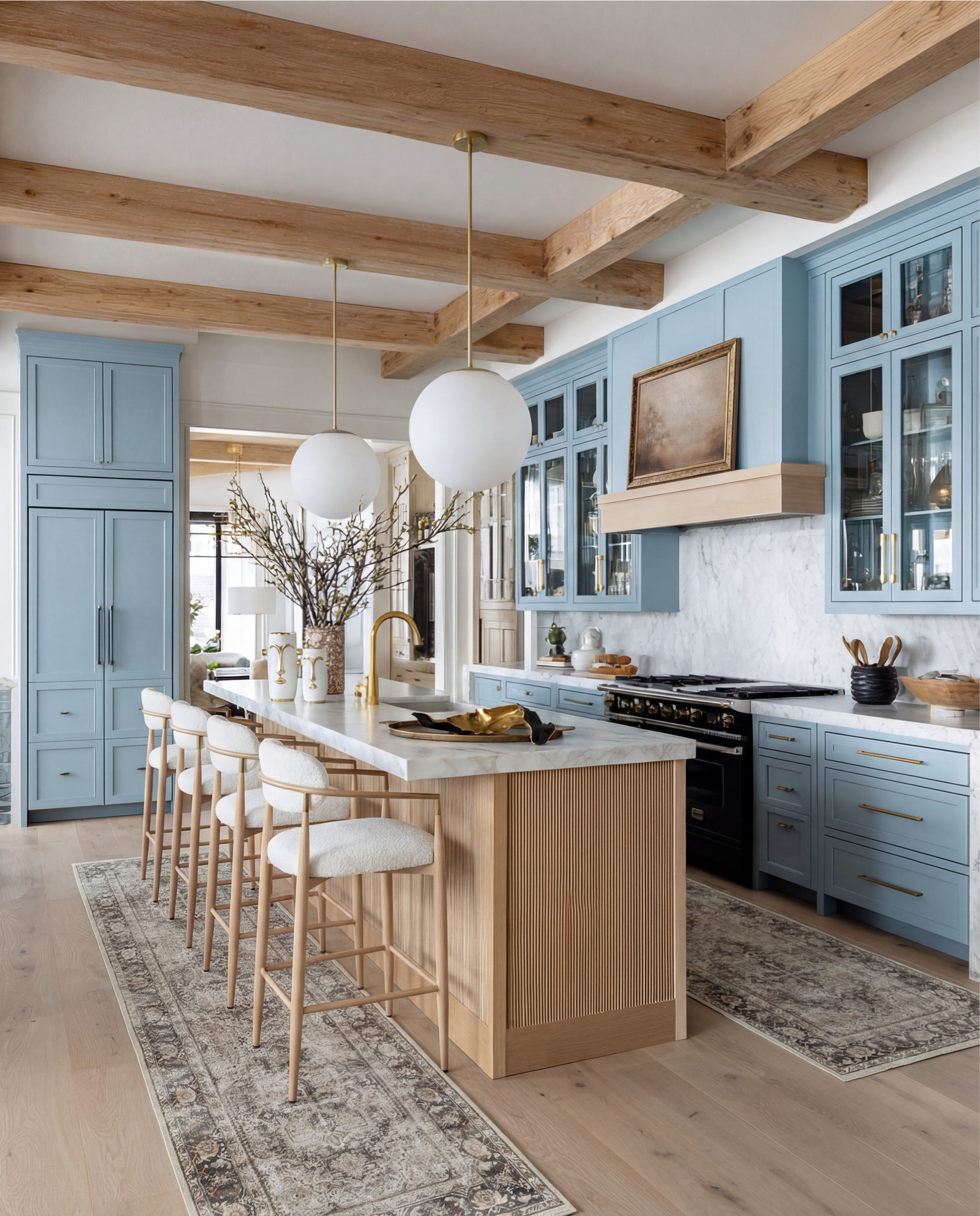 This kitchen is the definition of soft luxury with intention. Muted blue cabinetry sets a calm, timeless foundation, while the warm white marble countertops keep everything feeling light and elevated. The slatted wood island detail adds just the right amount of texture—subtle, architectural, and very designer-approved.

Those oversized globe pendants? A moment. They float above the island and balance the warmth of the exposed wood ceiling beams beautifully. Brass accents are layered throughout—from the faucet to the hardware—giving the space a collected, high-end feel without being flashy.

And the styling is where it really shines: sculptural gold bowls, organic wood trays, and dried florals that feel effortless but curated. This is one of those kitchens that looks lived-in, styled, and ready for hosting all at once.

Shop the Look:
• Soft blue shaker-style kitchen cabinets
• White marble countertops & backsplash (warm veining)
• Slatted wood kitchen island paneling (light oak)
• White globe pendant lights (brass stem)
• Brass kitchen faucet + brass cabinet hardware
• Boucle counter stools with light wood frame
• Black gas range
• Vintage-style runner rugs (neutral taupe + faded pattern)
• Sculptural gold decorative bowls
• Wooden serving tray (warm walnut tone)
• White sculptural ceramic vases with dried florals
• Glass vase with branch arrangement

#LTKFindsUnder100 #LTKSaleAlert #LTKHome