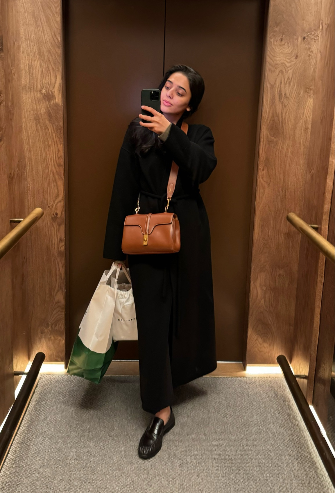 Longline black coat, gathered penny loafers, crossbody bag, tailored trousers, green cardigan