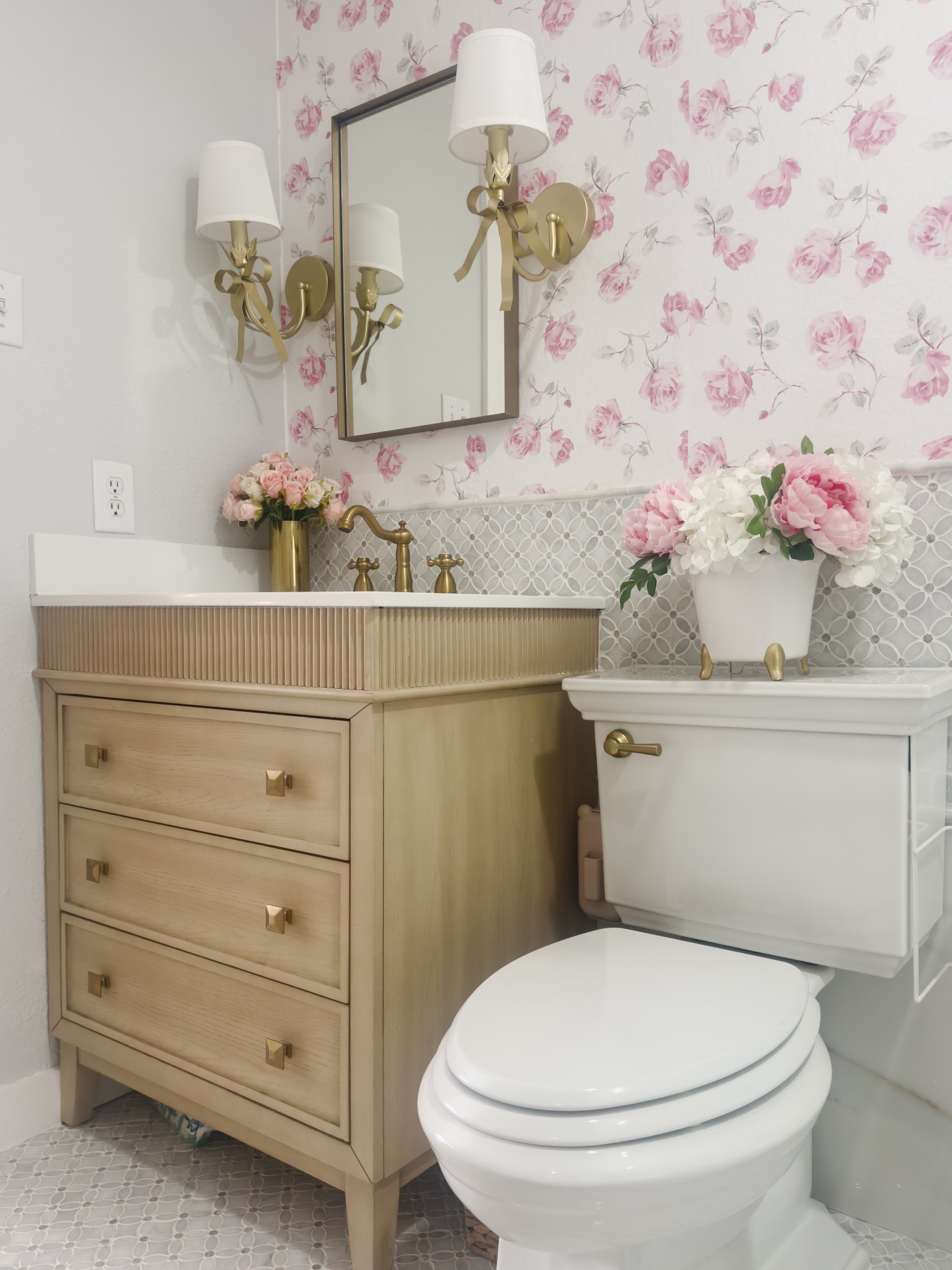 Florals, brass, and warm wood tones—this little bathroom got the sweetest refresh! I paired soft pink Loveshack Fancy rose wallpaper with a reeded wood vanity, brass mirror, and bow sconces for a space that feels elegant but fun.

What I used:
– Loveshack Fancy Rose wallpaper (removable)
– Fluted wood vanity with brass knobs
– Bow arm brass sconces
– Gold faucet + toilet lever for the finishing touch
- new stylish toilet#BathroomMakeover #PowderRoomInspo #FloralWallpaper #ClassicWithATwist #BrassFixtures #ReededVanity #FeminineDesign

#LTKHome #LTKHome #LTKSeasonal #LTKStyleTip