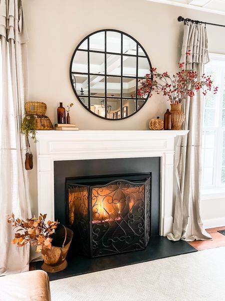 Fireplace mantel decorated for fall with vintage amber bottles and faux fall stems. Large round mirror with black metal mullions is perfect over a fireplace, in an entryway or foyer, and in hallways. This mirror is great in bedrooms and bathrooms too! #fireplacemantle #mantledecor #falldecor 

#LTKhome #LTKunder100 #LTKSeasonal