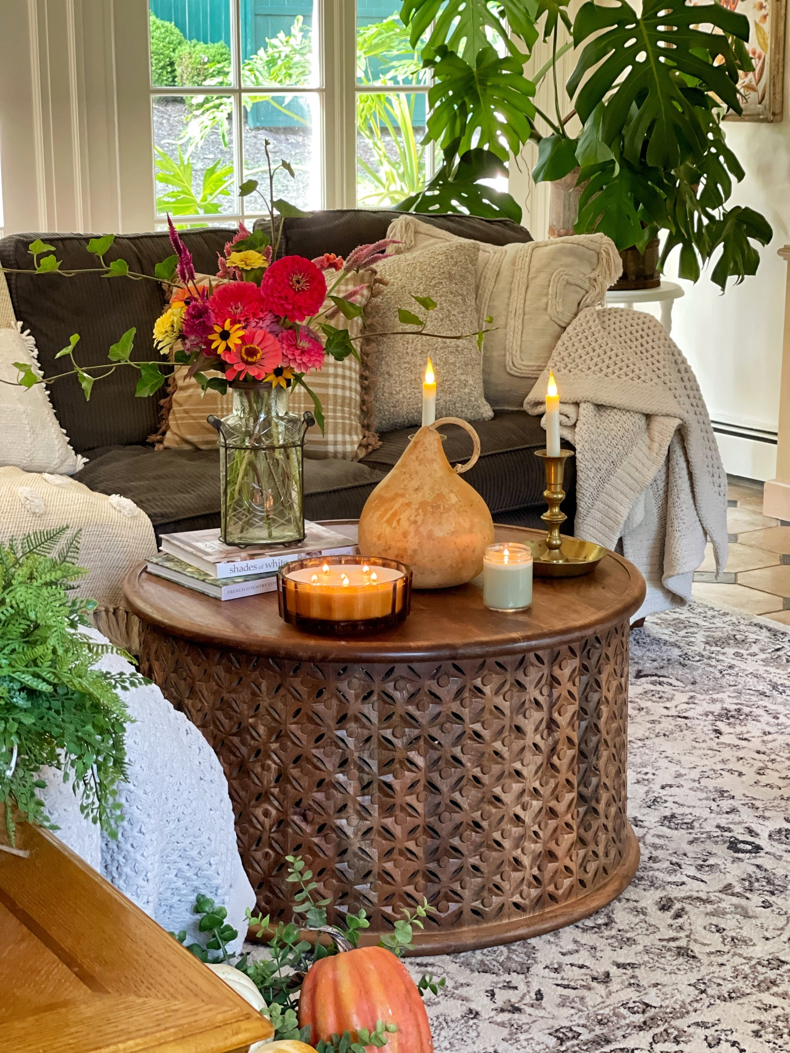 Cozy family room with fall decorations, boho farmhouse, cottagecore, round coffee table, mango wood, gourds, candles, sectional sofa, throw pillows, throw blankets, plants