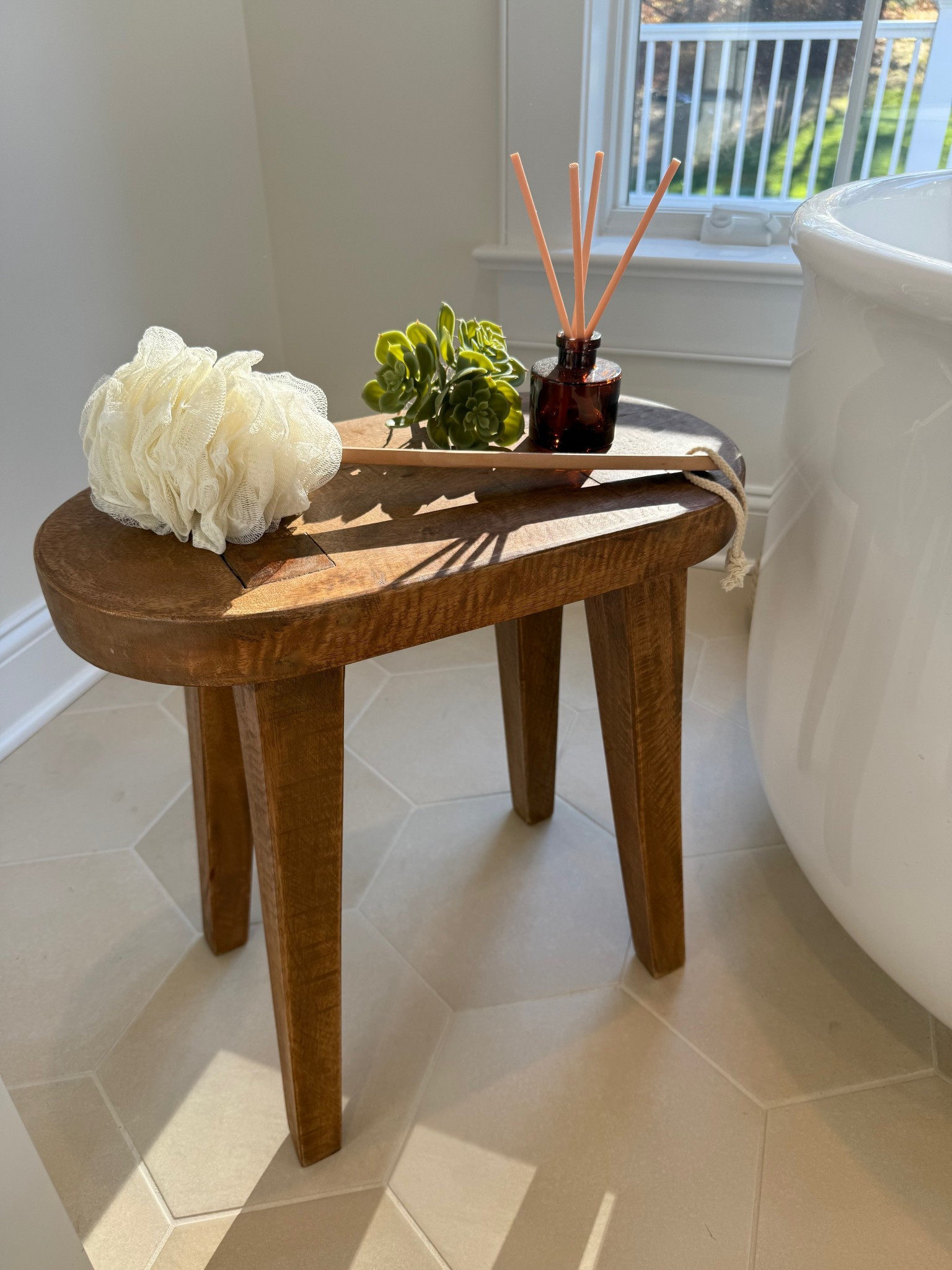 A close-up of the bathroom stool reveals its simple yet elegant design—crafted from natural wood with clean lines and a smooth finish. Positioned beside the soaking tub, it adds both warmth and practicality to the space, perfect for holding a towel or candle. The organic texture of the stool beautifully complements the serene tones and spa-like ambiance of the bathroom.