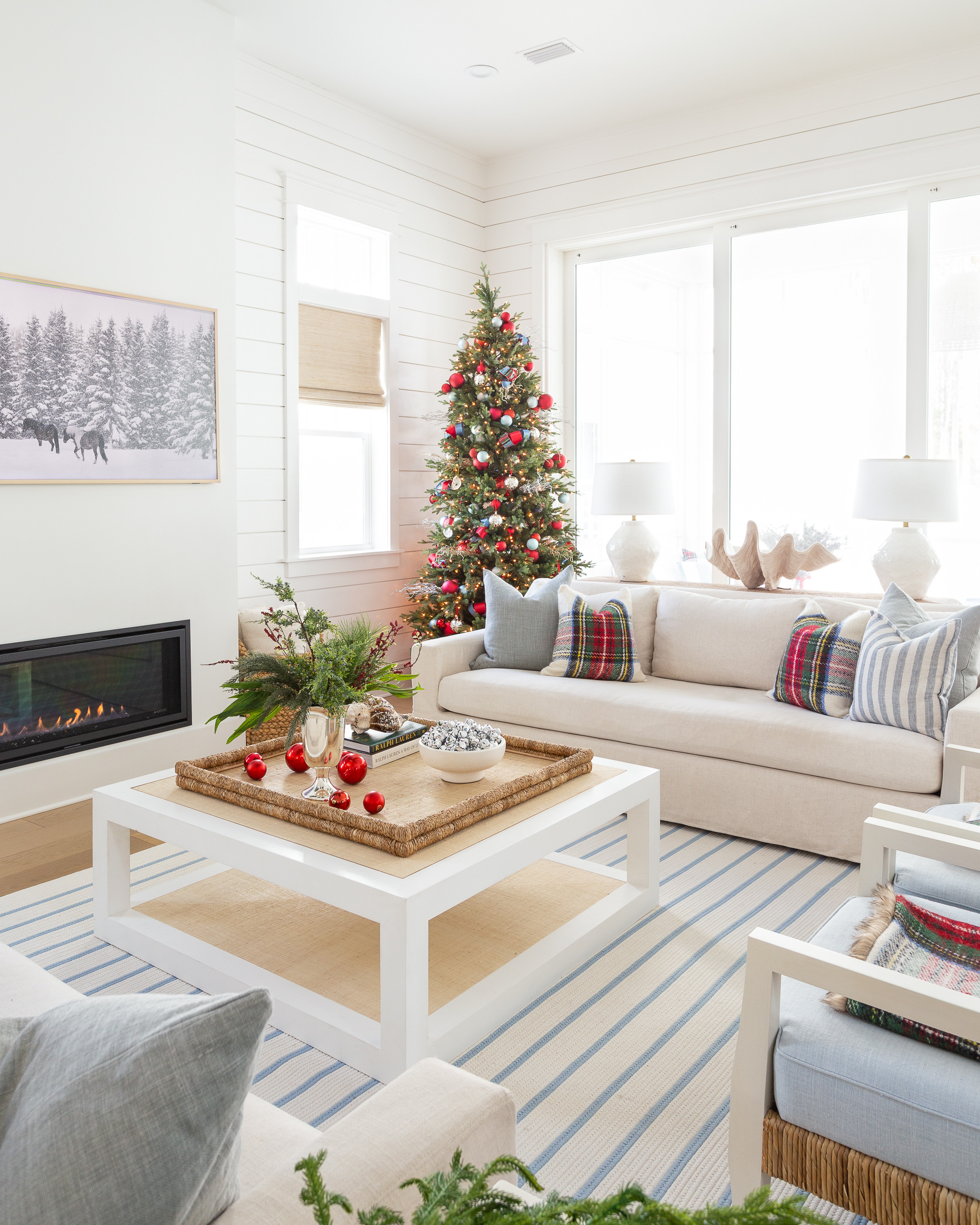 Our cozy coastal Christmas living room with linen sofas, blue and white striped rug, red Stewart plaid throw pillows, a 9' Christmas tree with red and silver ornaments, evergreen stems in a silver trophy vase, a raffia coffee table and cozy throw blankets. #ltkholiday #ltkhome #ltksalealert #ltkfindsunder50 #ltkfindsunder100 #ltkstyletip #ltkseasonal 

 

#LTKHoliday #LTKSaleAlert #LTKHome