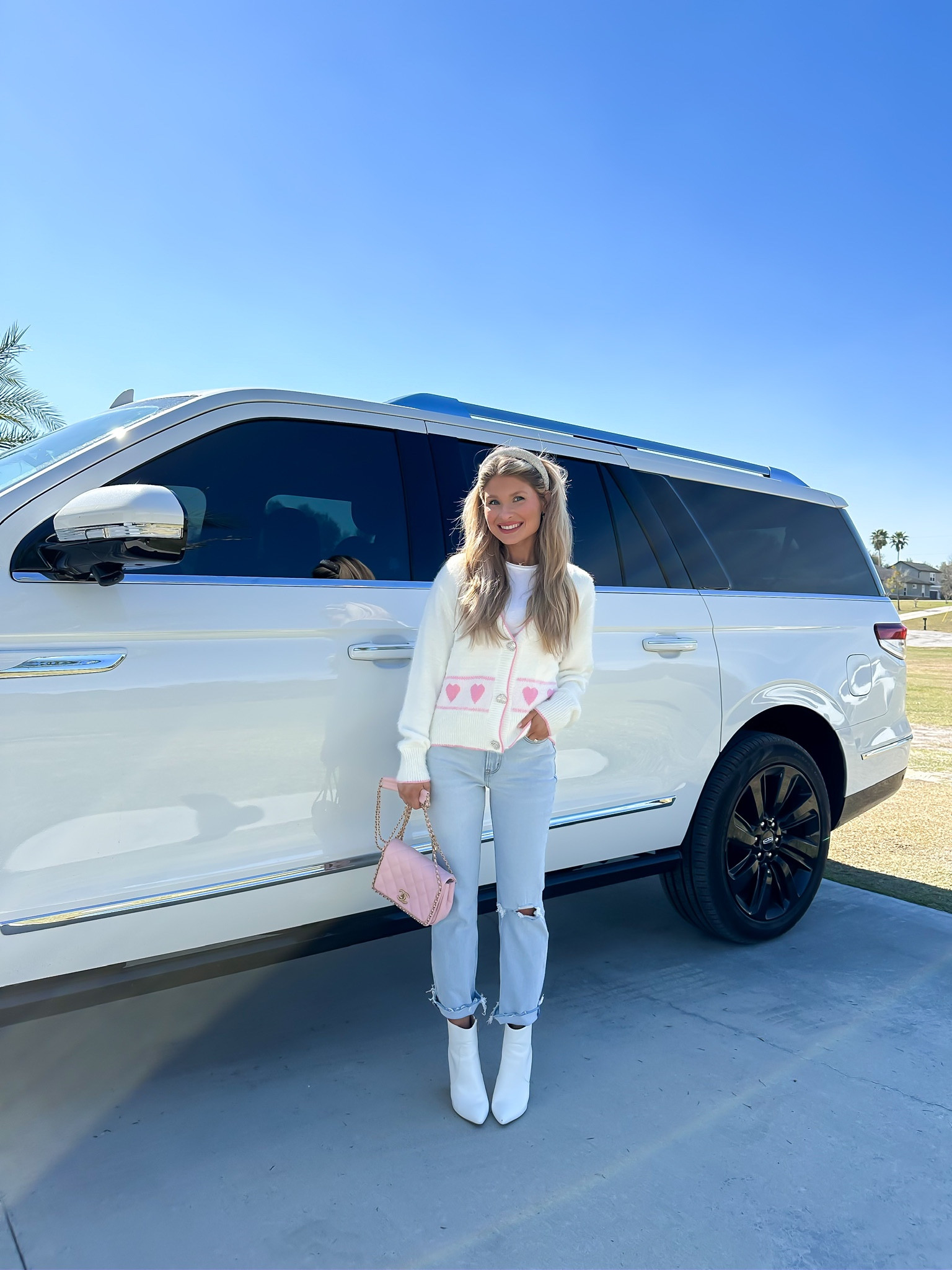 Valentine’s Day outfit info. Heart cardigan. White cardigan. Preppy style. Preppy cardigan. Spring style. White booties. Pink handbag. Mom style. Trendy outfit.