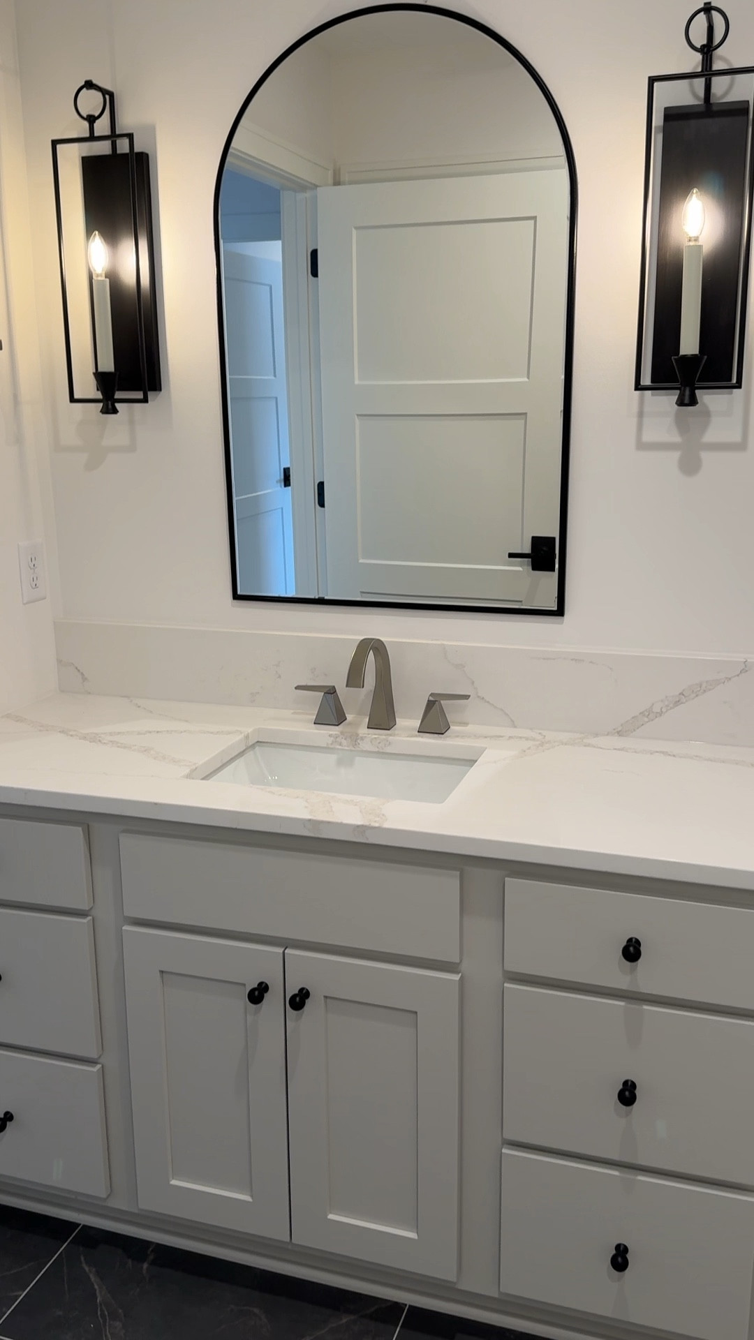 Sconces, an arched mirror and contrasting cabinet hardware and LVT flooring give this lower level bath lots of charm and character !

#LTKhome #LTKfamily #LTKSpringSale