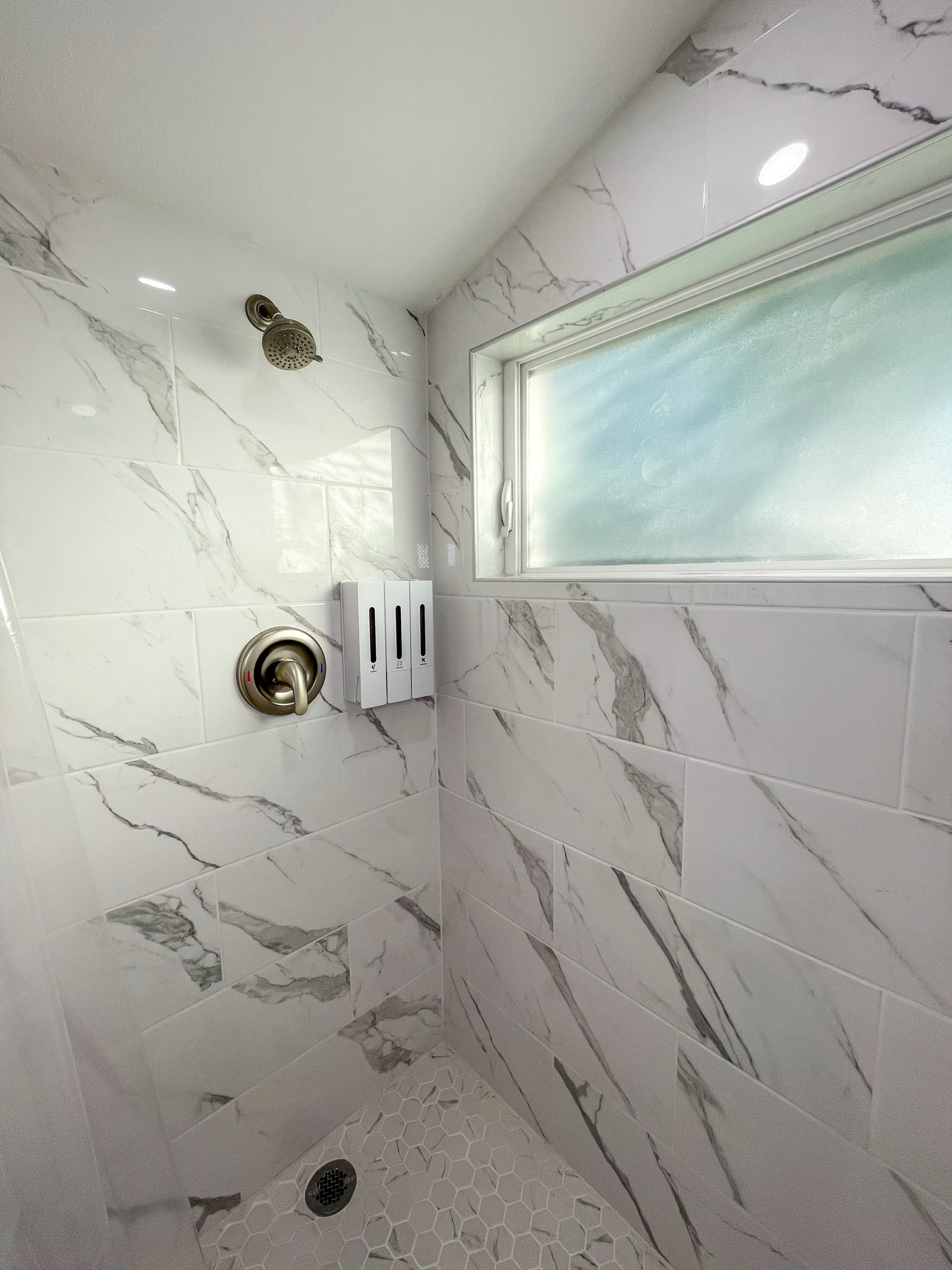 Marble tile shower with built-in dispensers for a hotel-style stay.