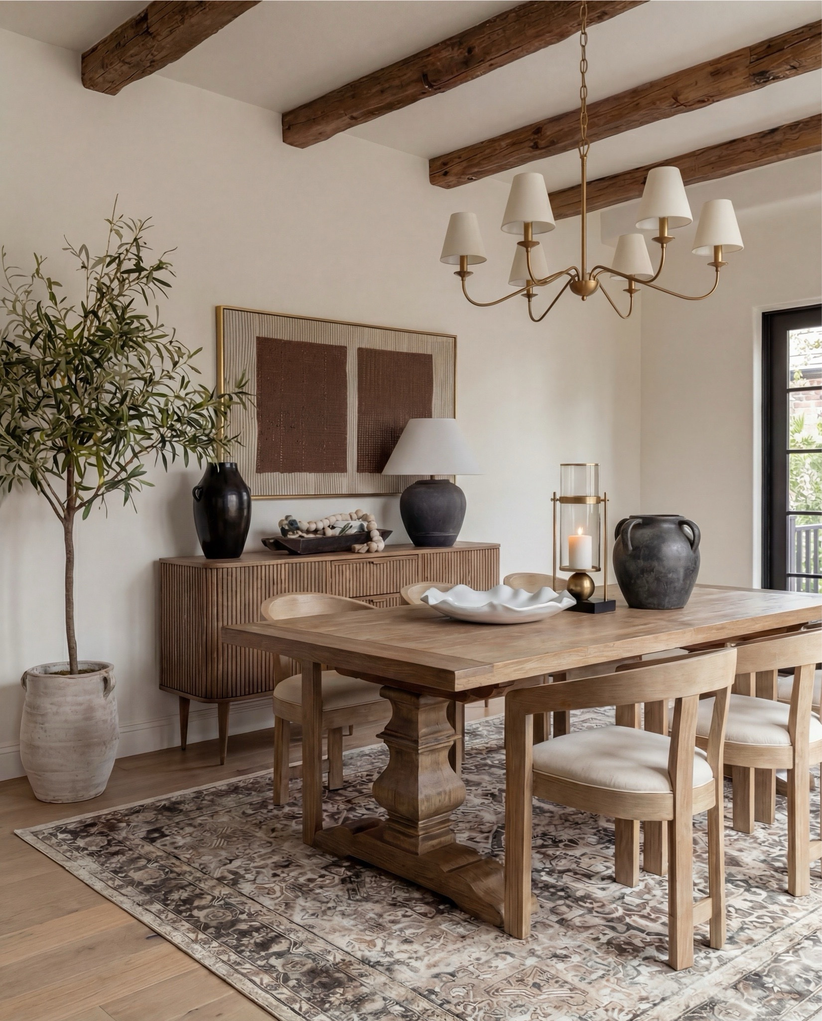 Shop the Look:
• Solid wood pedestal dining table (warm oak tone)
• Light wood dining chairs with upholstered seats
• Neutral vintage-style area rug (soft brown pattern)
• Brass chandelier with tapered fabric shades
• Exposed wood ceiling beams
• Large wood and glass display cabinet
• Fluted wood sideboard cabinet with brass hardware
• Black ceramic table lamp with linen shade
• Framed neutral textile wall art
• Matte black decorative vase
• Wood bead garland with tassels
• Decorative wood tray with ceramic bowl
• Small abstract sculpture decor
• Olive tree in stone planter
• White scalloped ceramic centerpiece bowl
• Dark ceramic pitcher vase (table decor)
• Glass hurricane candle holder
• Sheer neutral curtains



#LTKSaleAlert #LTKHome