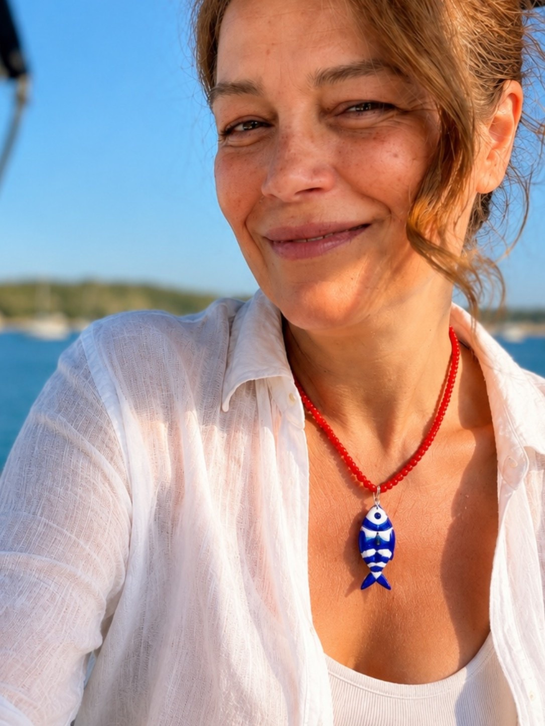 The necklace does all the talking. Vibrant coral-red beads paired with a blue-and-white  fish pendant create the perfect balance of playful and chic. Inspired by the Mediterranean coast, it’s the kind of statement accessory that transforms even the simplest white linen outfit into a summer look you’ll remember. Perfect for beach days, vacations, and anyone who loves effortless coastal style. 🐟