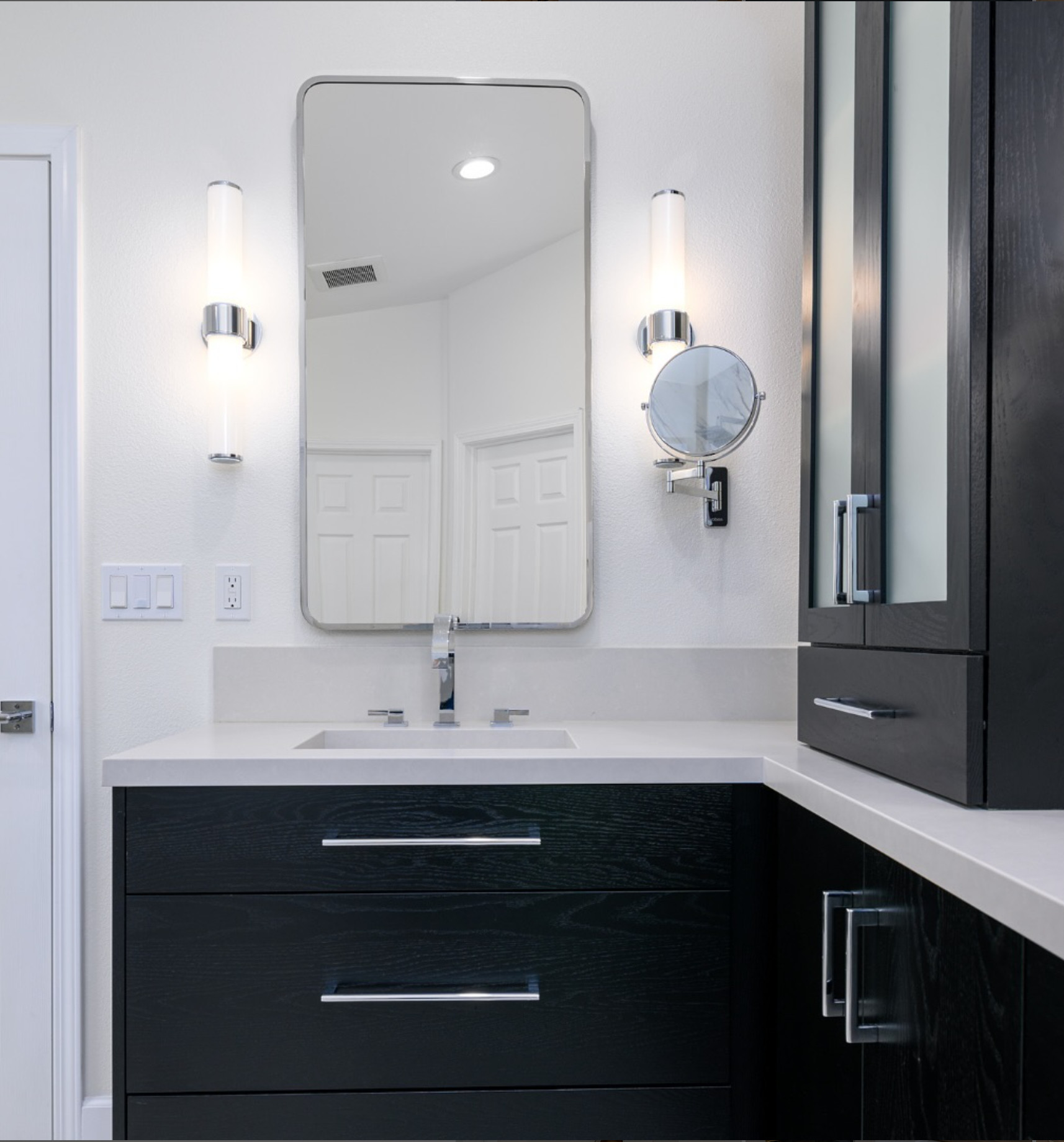 This bathroom remodel features striking black wood grain vanity cabinets paired with the timeless elegance of chrome hardware. The matching chrome mirror and frosted glass sconces add a modern touch while the crisp light gray countertop brings balance and brightness. A perfect blend of bold and refined. 

 #LTKHome