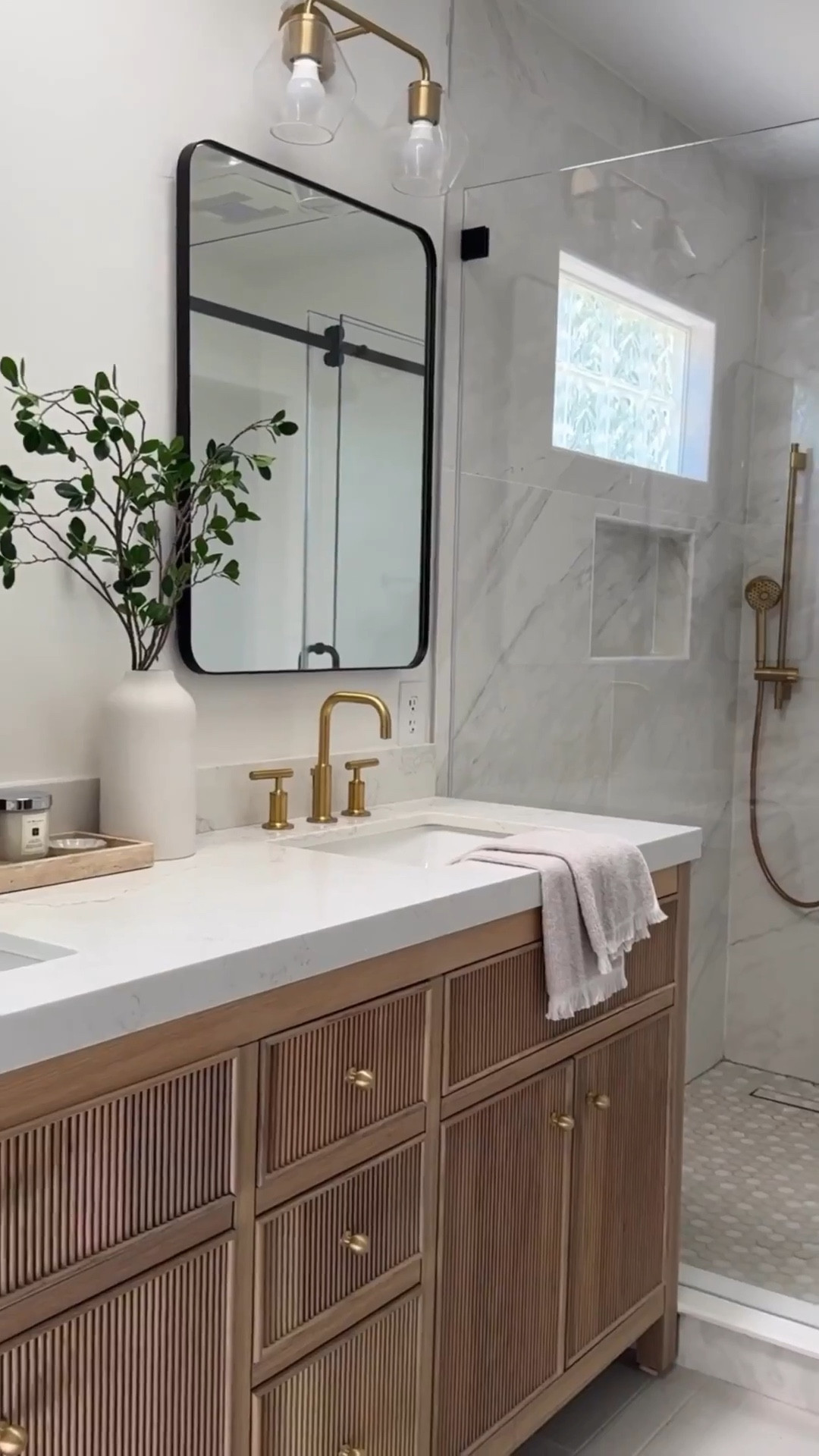 This entire beautiful bathroom is from Wayfair and they're having sale!
We used so many affordable options, yet were able to achieve this high-end look.
Love the reeded detail of this prefab wood vanity, which comes with multiple different countertop options. My favorite part could be the medicine cabinet. So stylish and functional. Love how the neutral colors of the tile provide a serene vibe.
Marble tile, large format, tile, gray tile, wood, vanity, brass faucet, brass shower system, black rectangle, mirror, medicine cabinet glass, sconces, brass, sconces, glass, shower door, sliding glass door.

#LTKHome #LTKSaleAlert