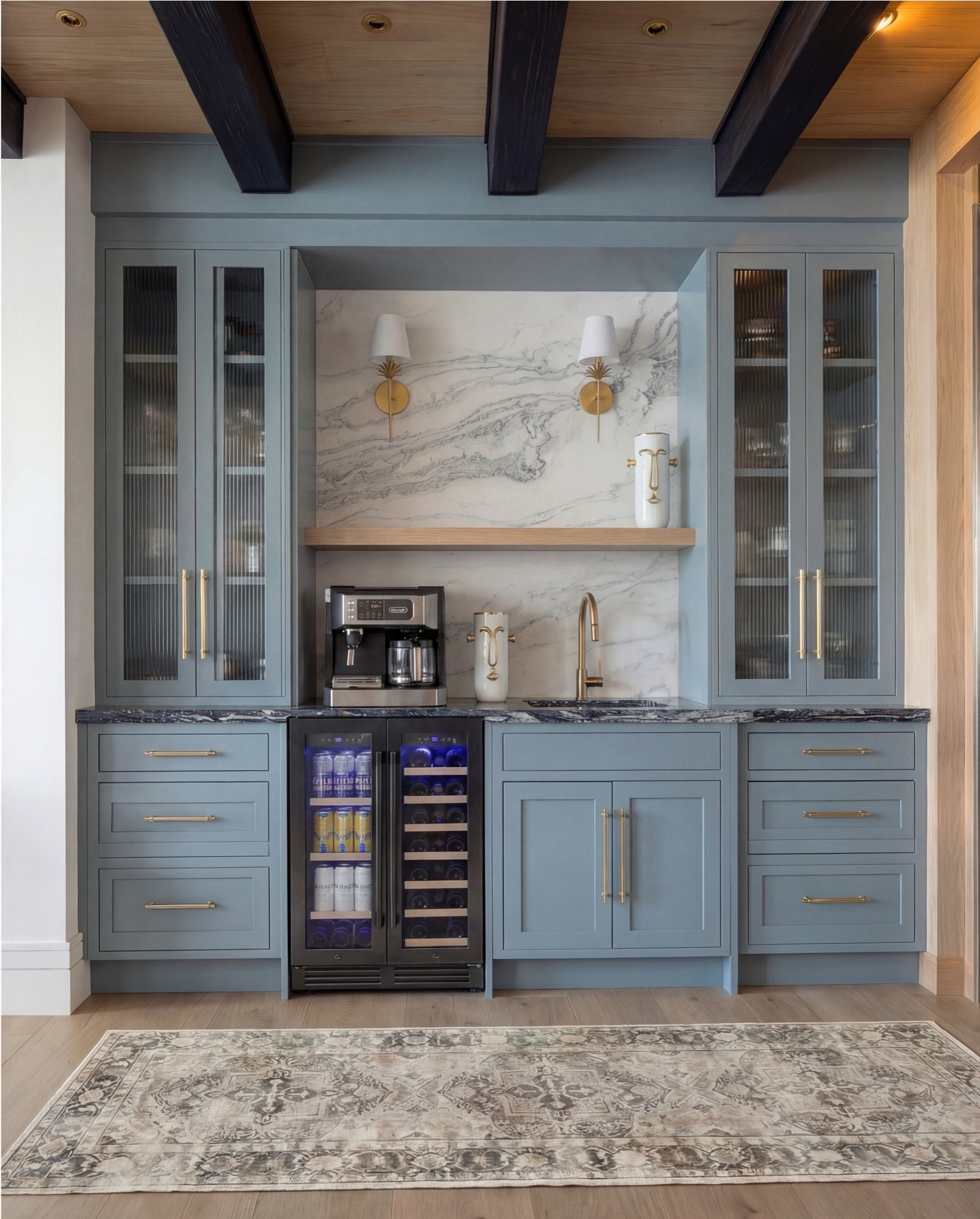 Shop the Look:
• Soft blue paneled cabinetry
• Brass cabinet pulls + drawer handles
• Fluted glass upper cabinet doors
• Marble slab backsplash (gray veining)
• Dark marble countertops
• Brass wall sconces with white shades
• Built-in beverage fridge
• Built-in wine fridge
• Stainless steel coffee maker
• Brass gooseneck bar faucet
• Undermount bar sink
• Light wood floating shelf
• Decorative ceramic face vase (white + brass details)
• Wood ceiling with dark exposed beams
• Vintage-style runner rug (neutral pattern)
• Light wood flooring

#LTKHome #LTKSaleAlert