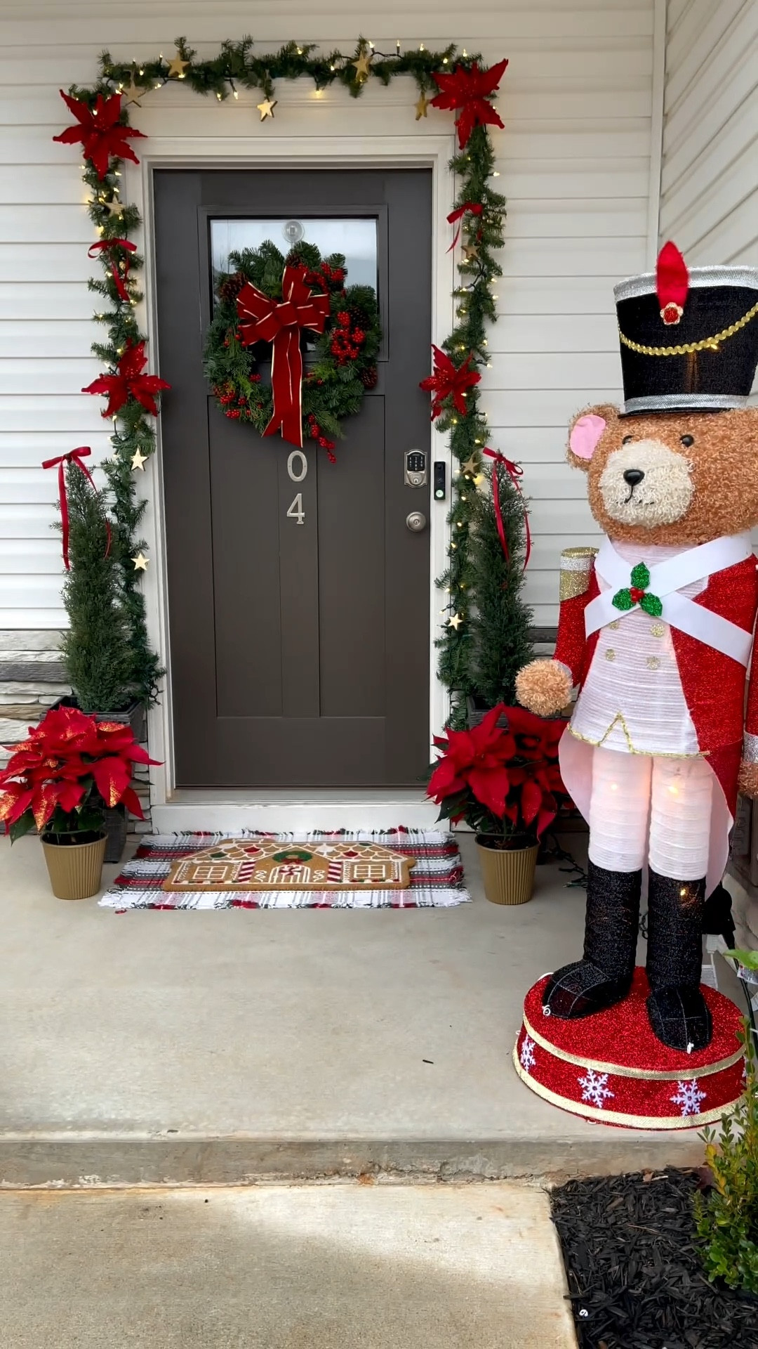 Christmas 2025 front porch decor. Trendy Christmas teddy bear wearing a nutcracker clothes. Real Poinsettias and beautiful cedar pines with red bows. I decided to add a garland under $3 (I used two) and added some vintage gold stars and faux poinsettias from Lowe’s 

#LTKHoliday #LTKHome #LTKFindsUnder50