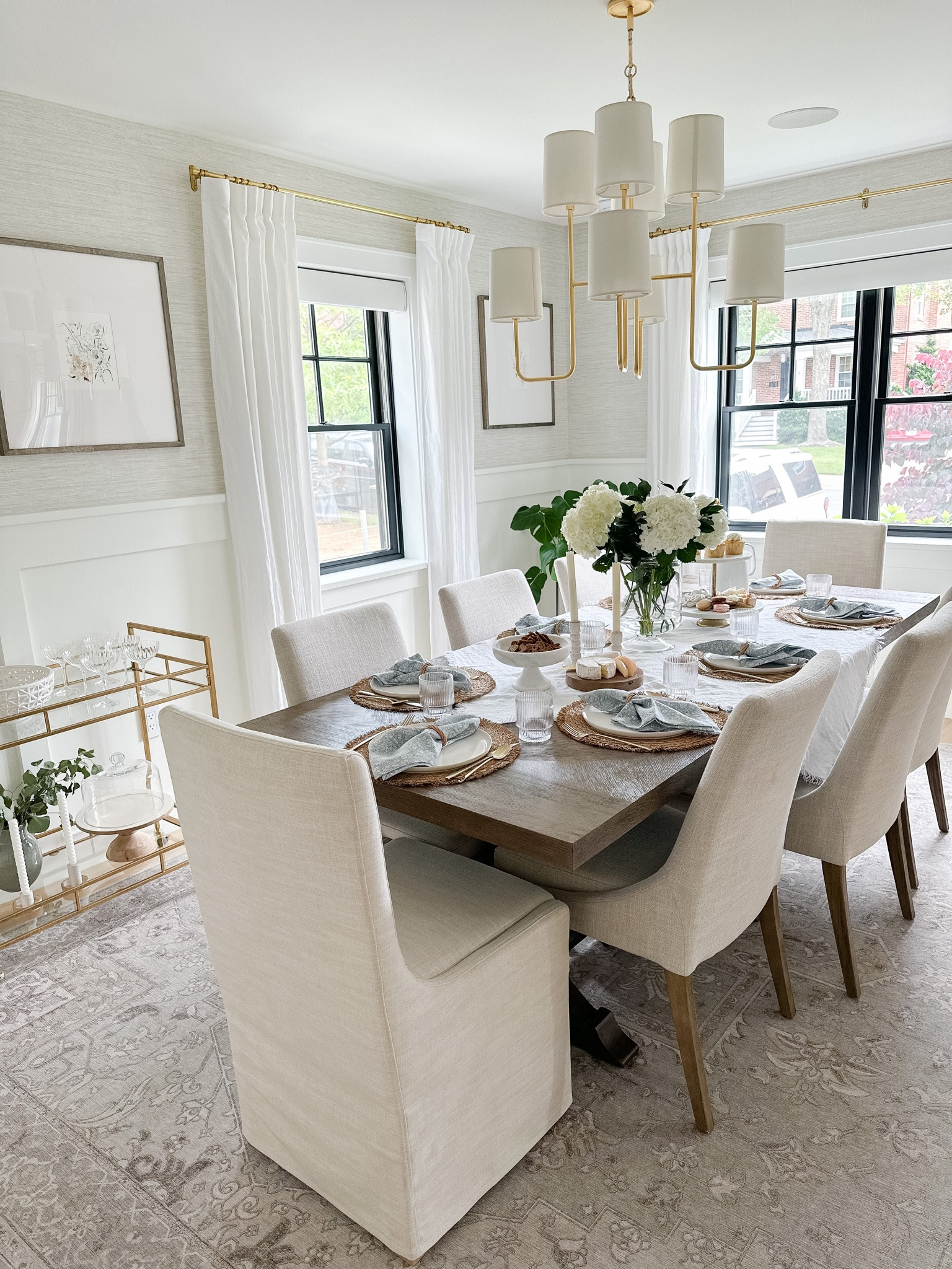 Dining room design. Upholstered dining chairs, parsons chairs, trestle dining table, brass chandelier, light gray neutral grass cloth wallpaper, gold bar cart, gallery frames 

#LTKstyletip #LTKhome #LTKsalealert