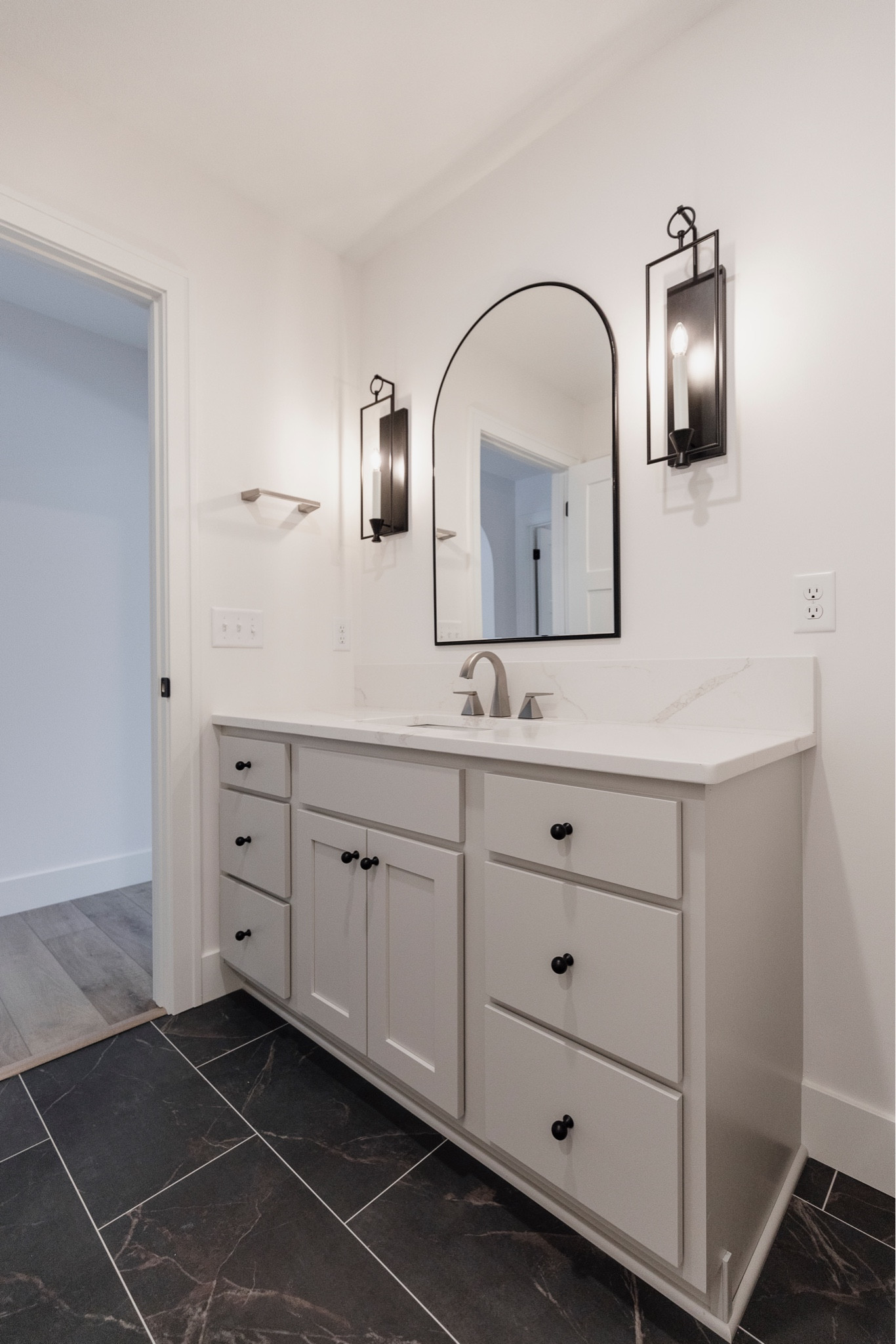 We love using sconces in bathrooms for more interest and character! It takes a little more planning in advance for rough-ins and making sure the sizing/location is accurate, but worth it. We paired it with an arch mirror, pretty quartz top and a contrasting LVT floor to complete this lower level bathroom! 😍

#LTKhome #LTKSpringSale