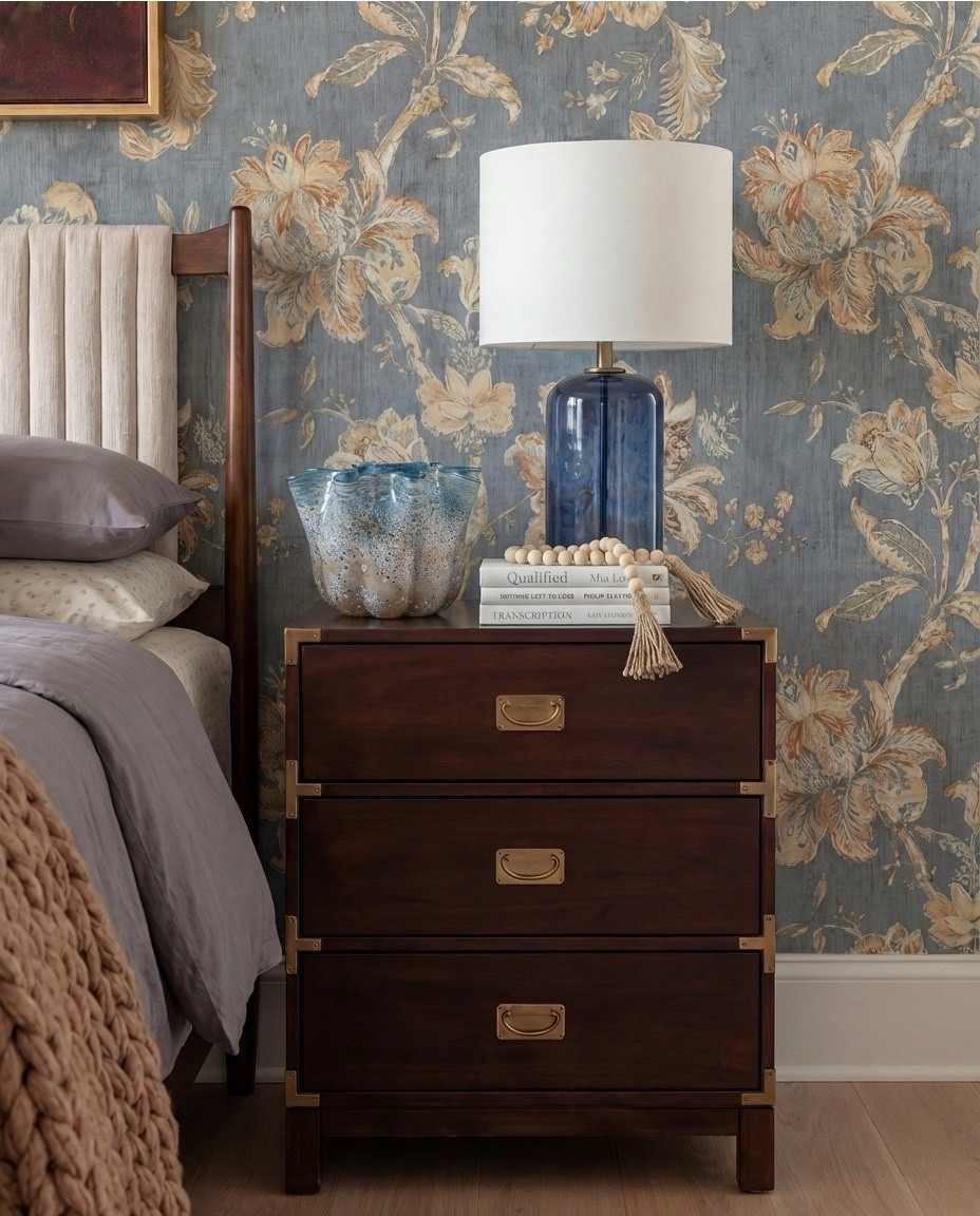 Shop the Look: Bedroom Refresh
• Warm-wood platform bed frame
• Vertical-channel upholstered headboard
• Gray duvet cover + layered sheet set
• Mixed blue + neutral accent pillows
• Oversized chunky knit throw blanket
• Shearling-style upholstered storage bench at the foot of the bed
• Pair of dark-wood campaign-style nightstands with brass hardware
• White drum-shade table lamps with blue glass bases
• Blue decorative bowls
• Bead garland décor
• Stack of books (nightstand styling)
• Framed oversized floral artwork above the bed
• Blue floral wallpaper (full wall + ceiling)
• Exposed wood ceiling beams
• Blue patterned area rug
• Window bench with plaid/tan accent pillows

#LTKHome #LTKSpringSale #LTKSaleAlert