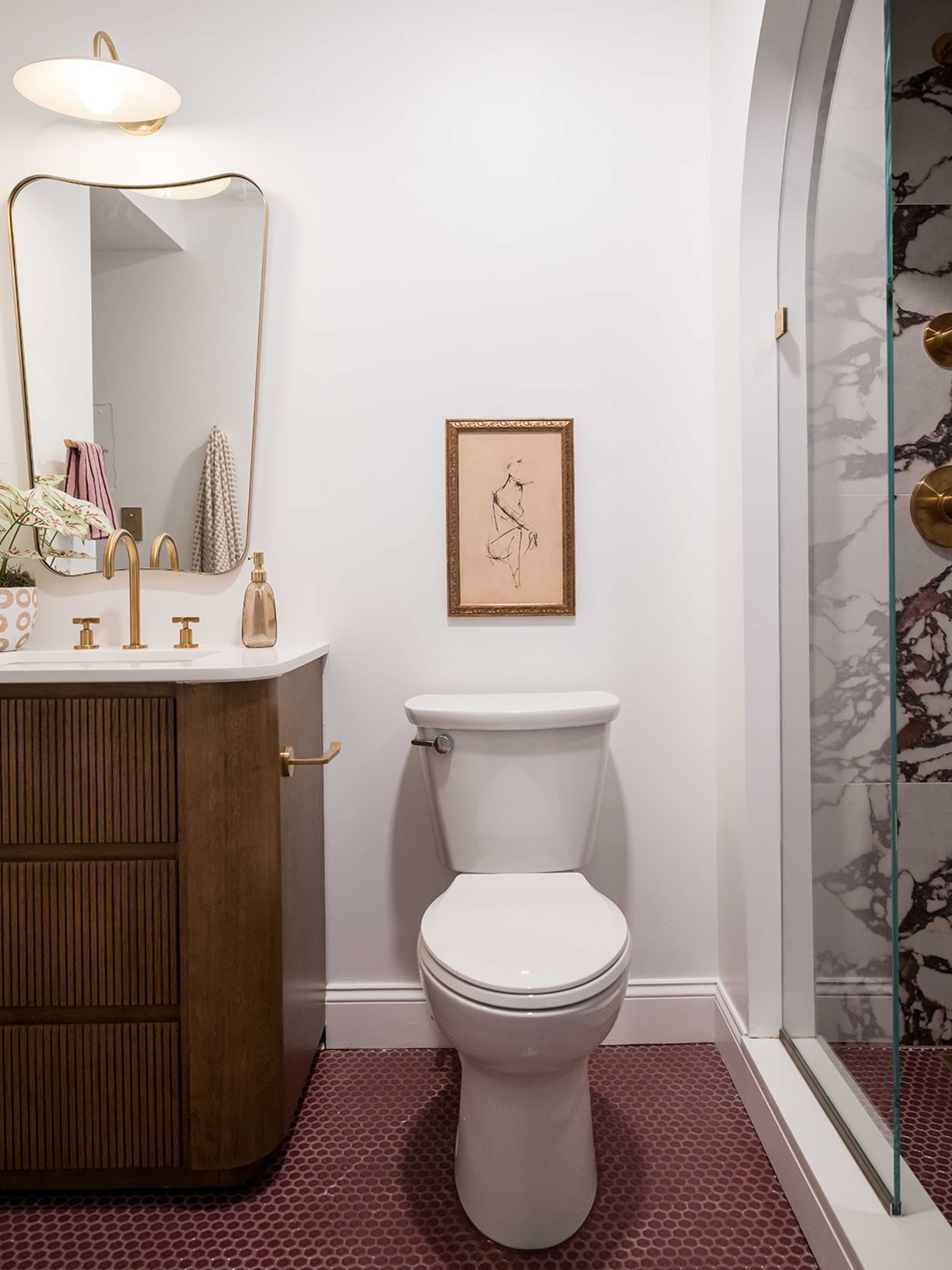 in contrast to the bright and airy bedroom space, #dwelloctoberstudio went with a moodier feel for the en suite bathroom, using deep plum penny tile for the floor, a Calacatta Viola-inspired tile for the shower walls, and a rich wood vanity. brushed gold plumbing fixtures and accessories add more warmth to the space, while caned doors camouflage a utility closet. #dwelloctober

#LTKHome